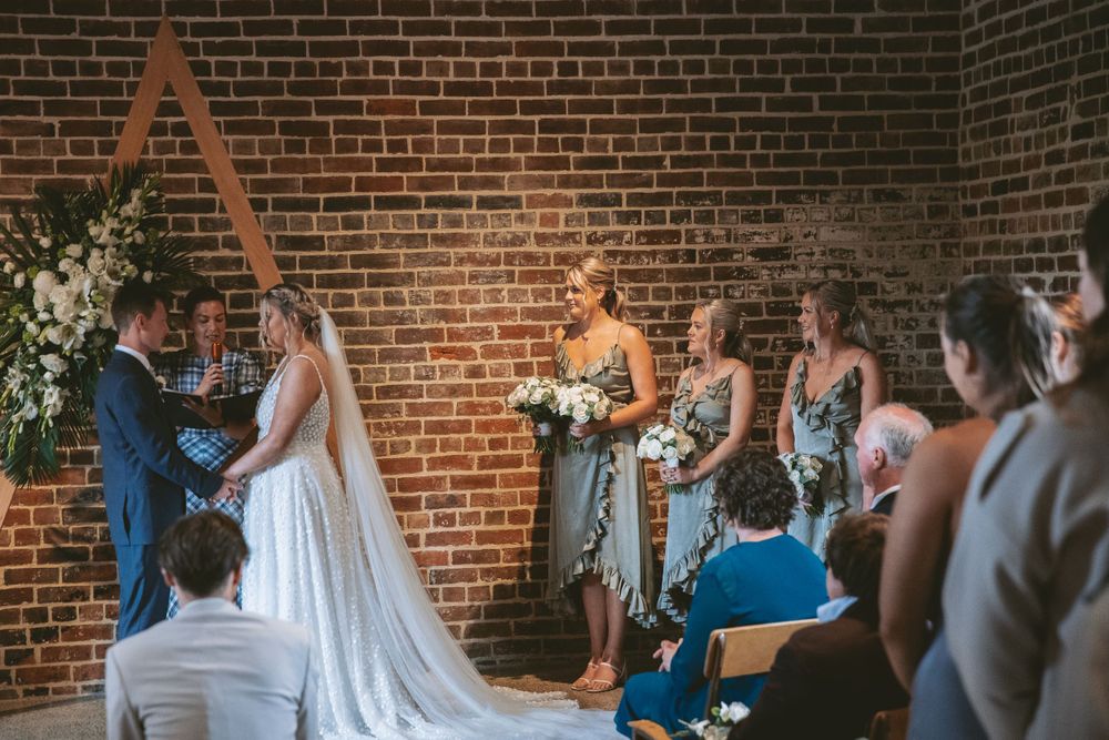 An intimate wedding ceremony unfolds in front of a wooden triangle arch with floral decorations.