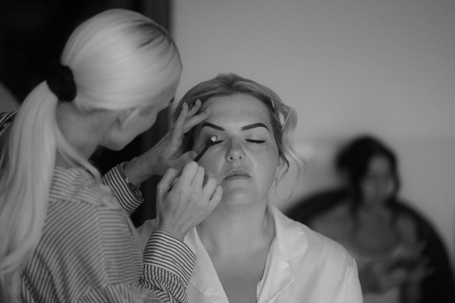 Black and white photograph of wedding makeup preparation in progress.