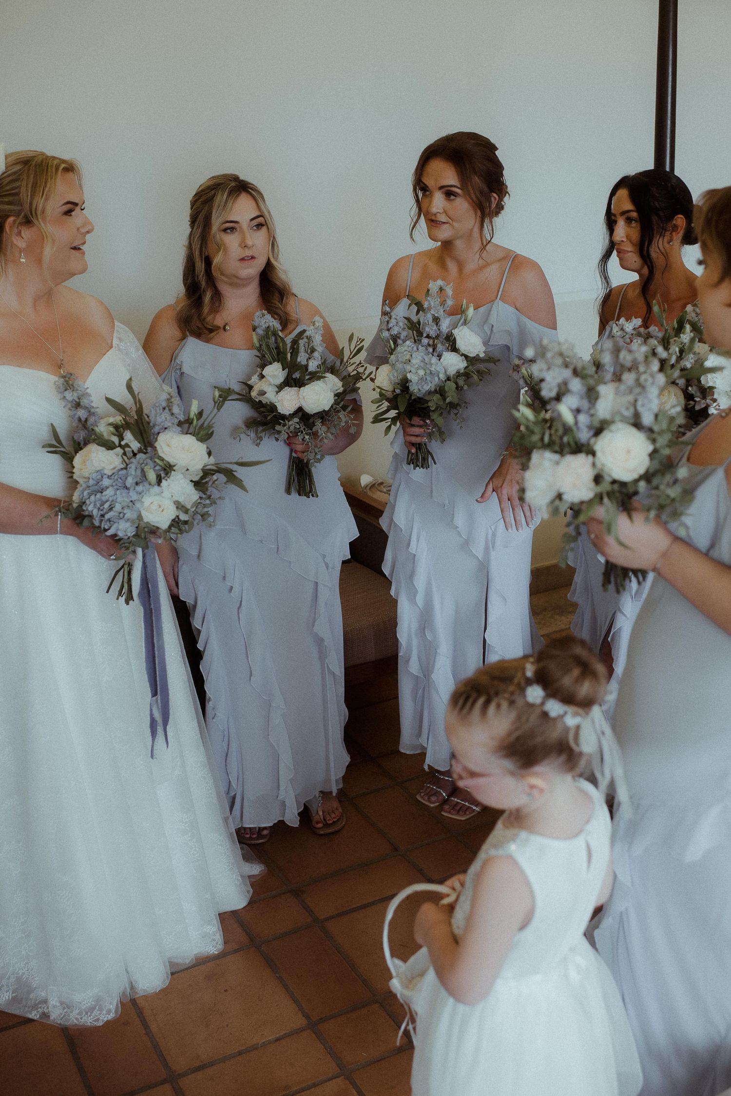 Bridesmaids in light colored dresses gather with flower girls holding matching bouquets.