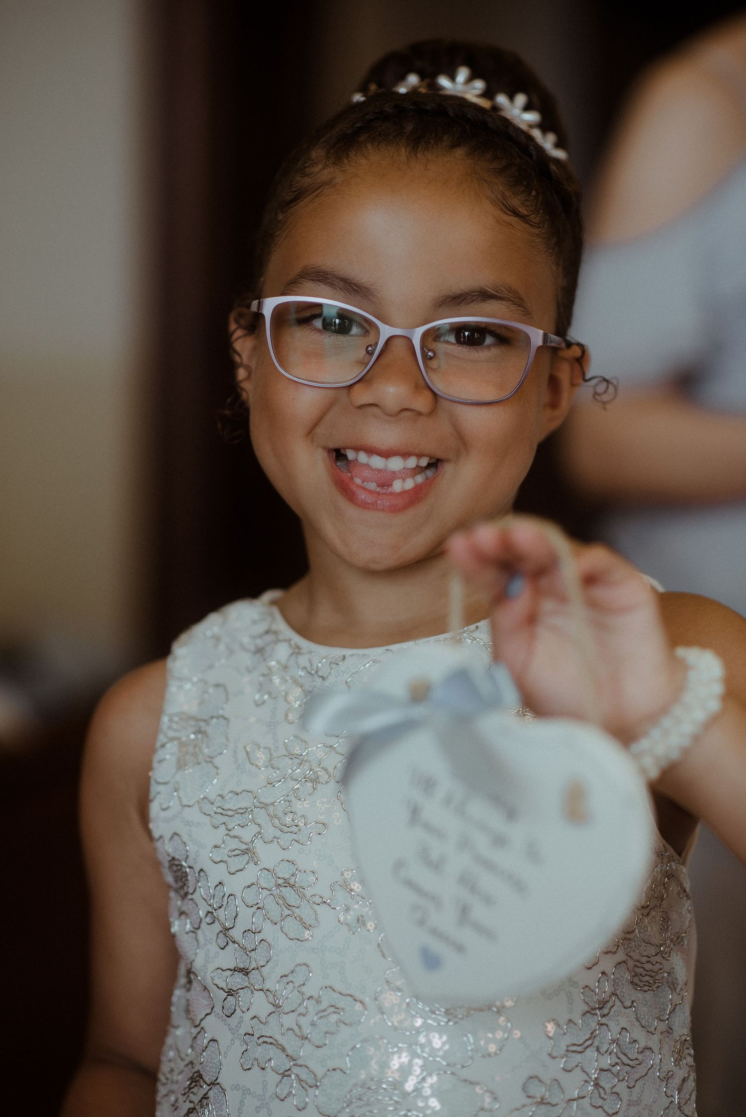 A young flower girl in white lace dress holds up a heart-shaped token.