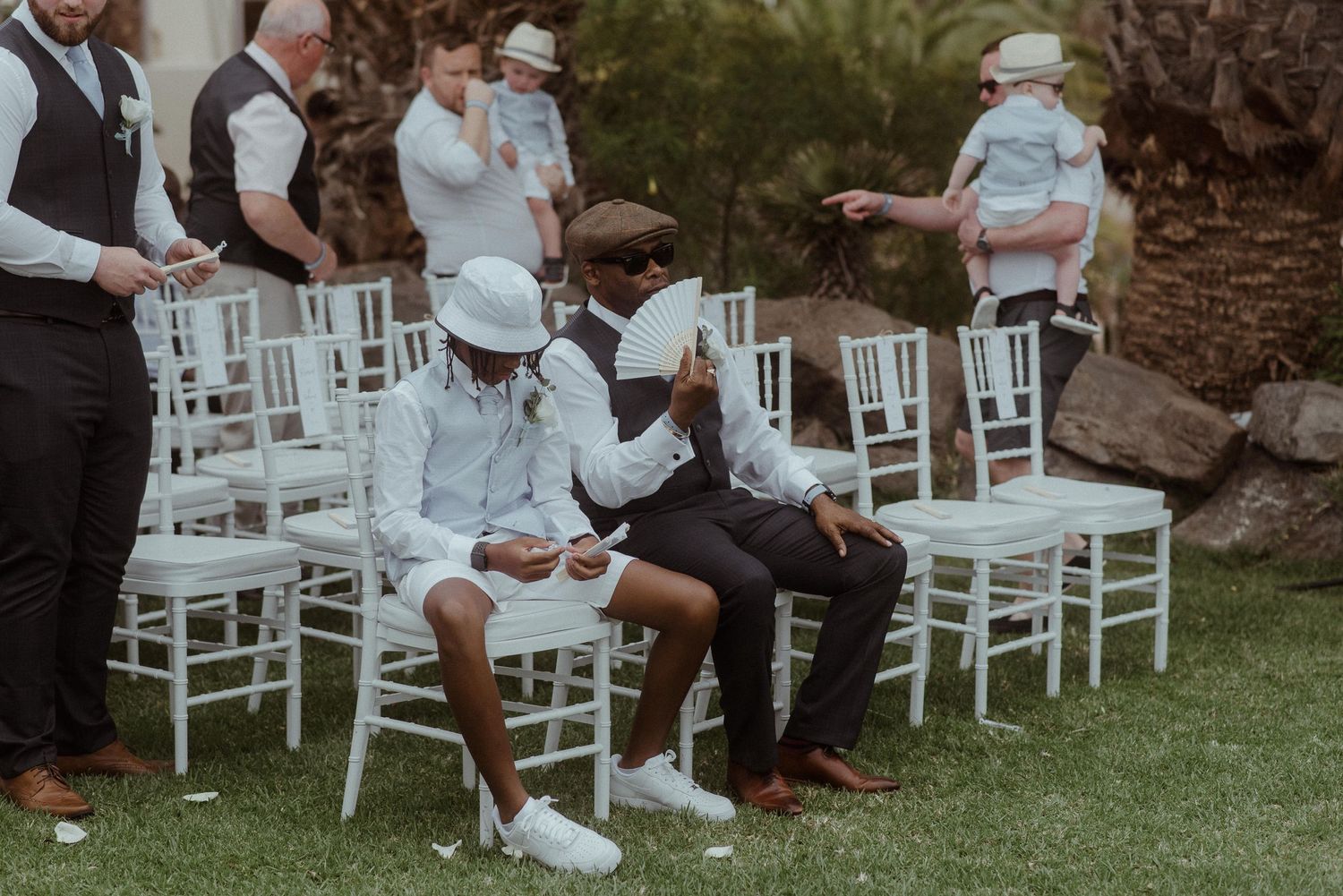 Wedding guests seated in white chairs on a manicured lawn during an outdoor ceremony.