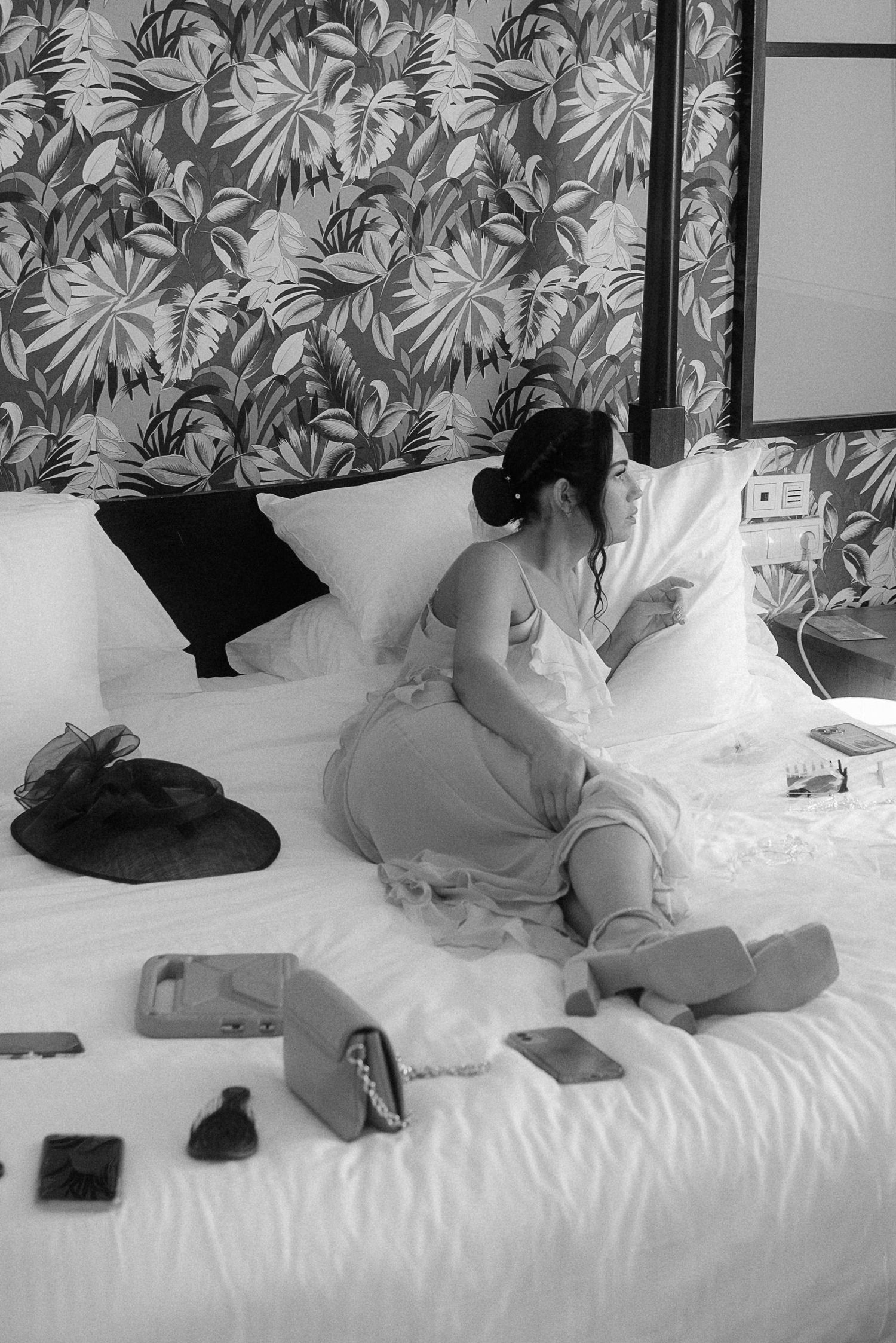 Wedding preparation scene with various items scattered on a white bed with floral wallpaper. Tenerife Wedding Photographer at Hotel Vincci