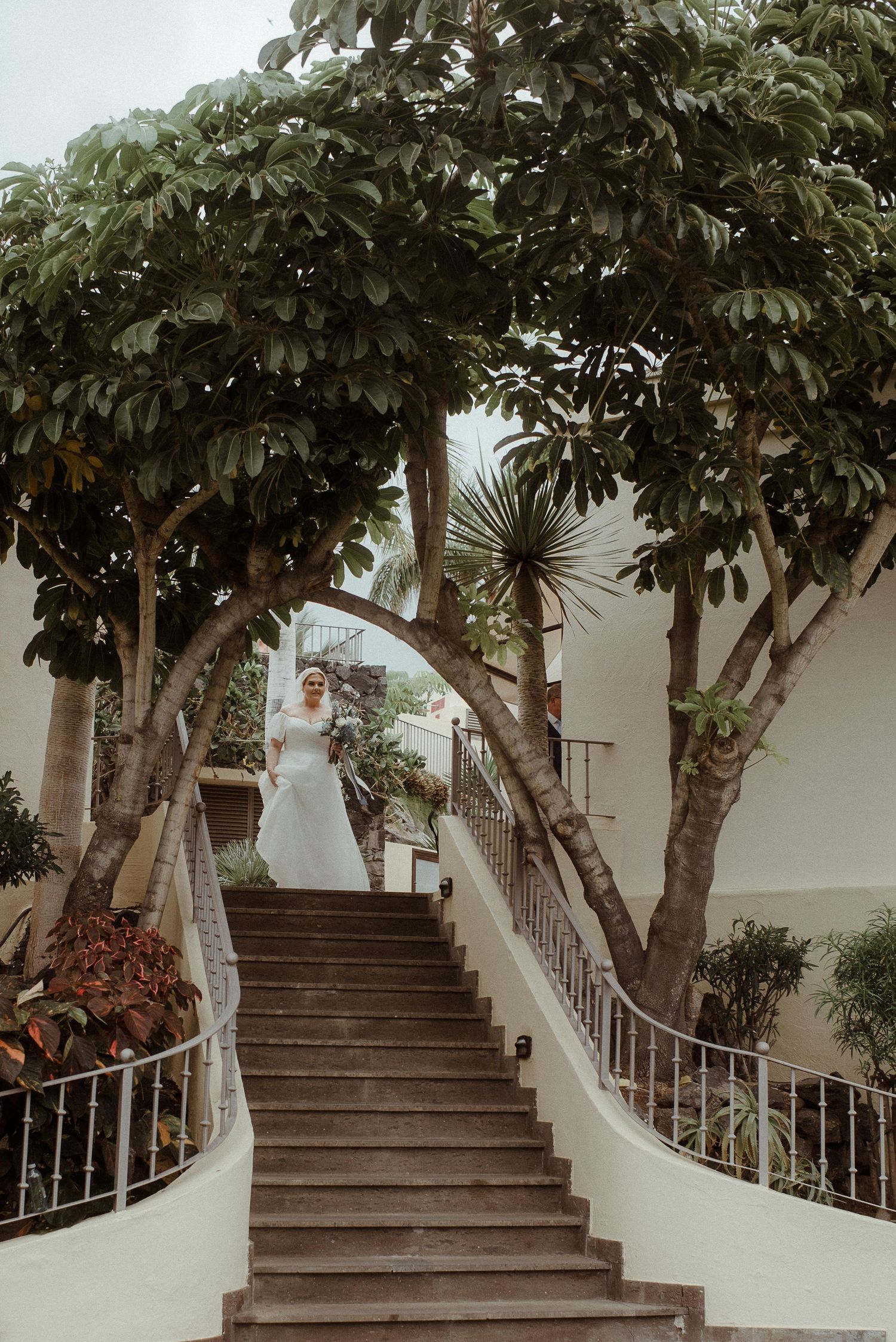 A grand white staircase framed by lush trees creates a romantic wedding ceremony entrance. Tenerife Wedding Photographer at Hotel Vincci