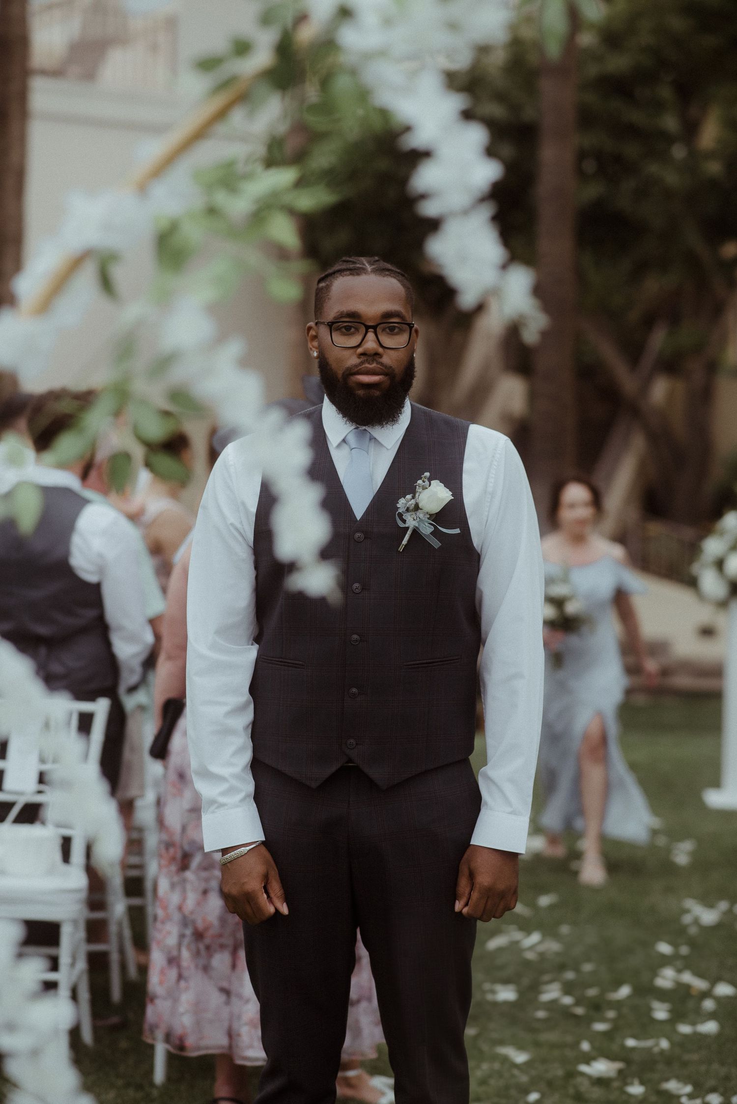 A formal wedding attendant in vest and tie poses among outdoor ceremony seating. Tenerife Wedding Photographer at Hotel Vincci La Plantación