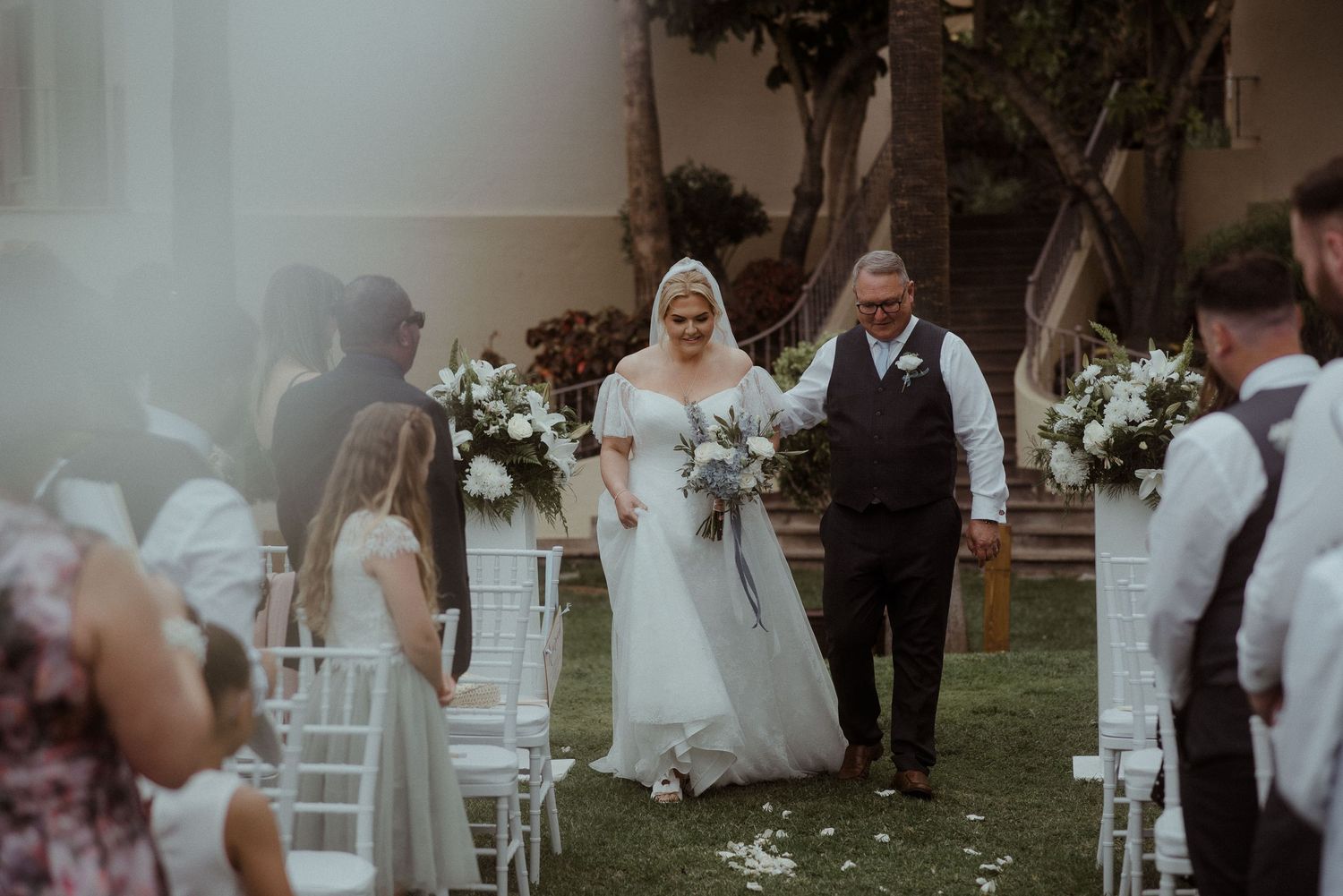 A wedding ceremony takes place on a grassy lawn with white chairs and floral decorations. Tenerife Wedding Photographer at Hotel Vincci