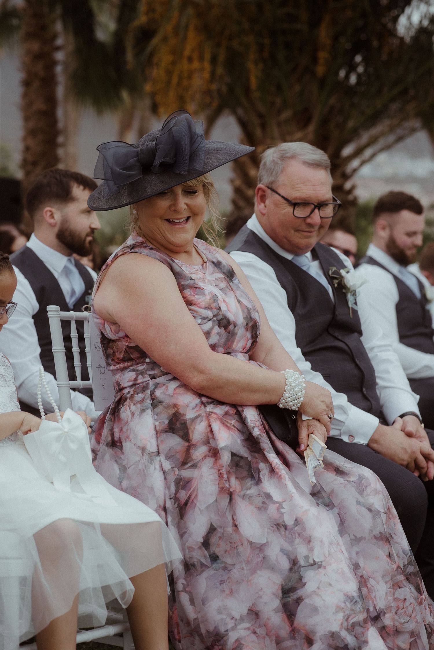 Wedding guest in floral dress and dramatic hat seated during ceremony. Tenerife Wedding Photographer at Hotel Vincci La Plantación del Sur