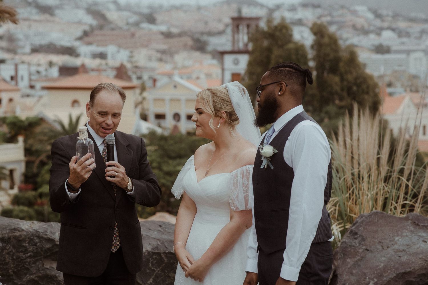 Outdoor wedding ceremony with three people gathered near a scenic hillside cityscape. Tenerife Wedding Photographer at Hotel Vincci