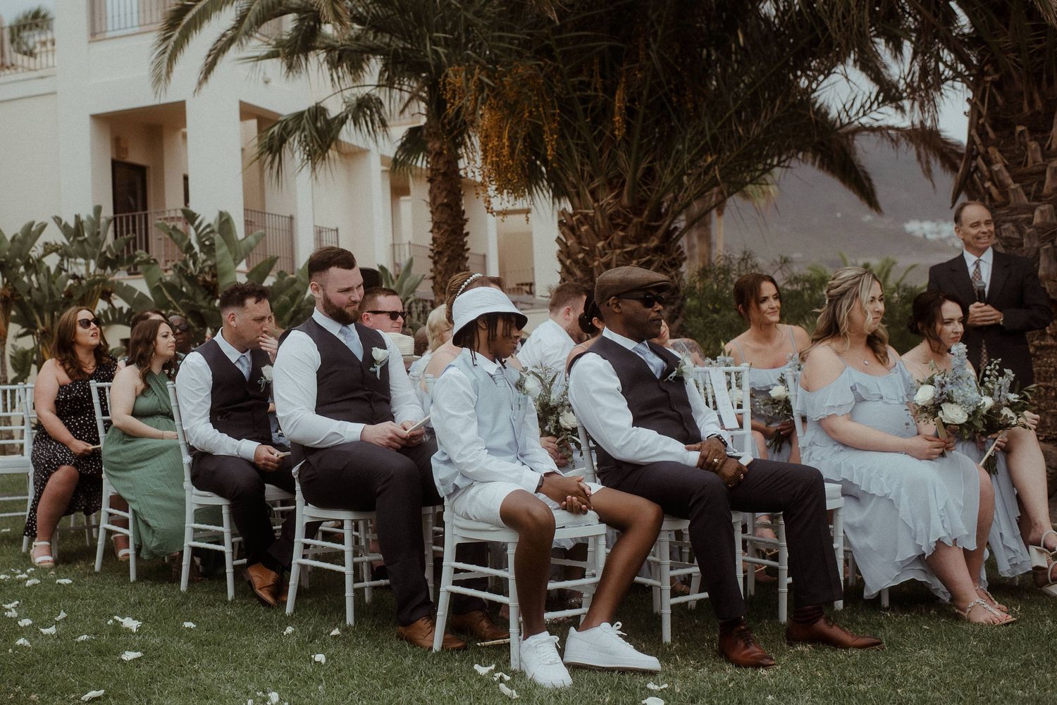 Wedding ceremony guests seated in rows on a garden lawn with palm trees. Tenerife Wedding Photographer at Hotel Vincci La Plantación del Sur