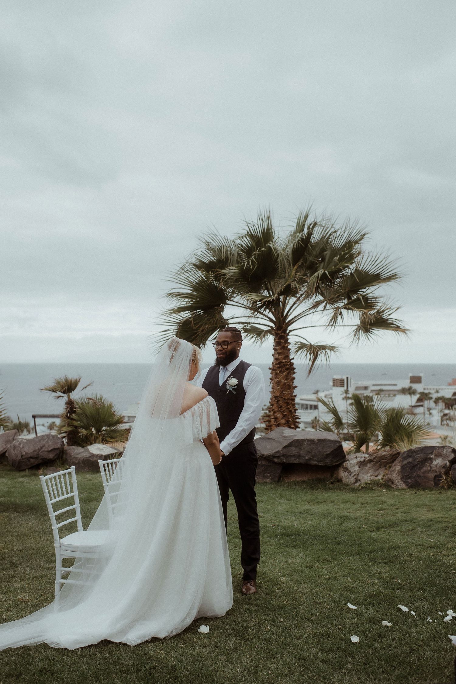 A couple shares their first kiss as newlyweds under a palm tree by the ocean on their wedding day. Tenerife Wedding Photographer at Hotel Vi
