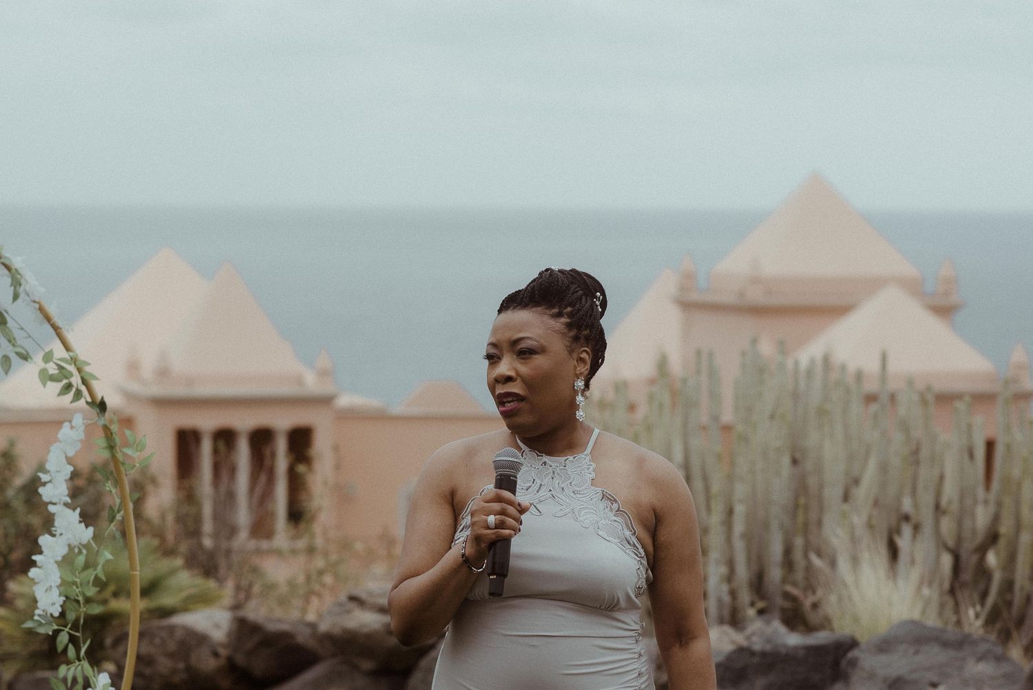 Wedding speaker stands at outdoor venue with coastal buildings in background.
