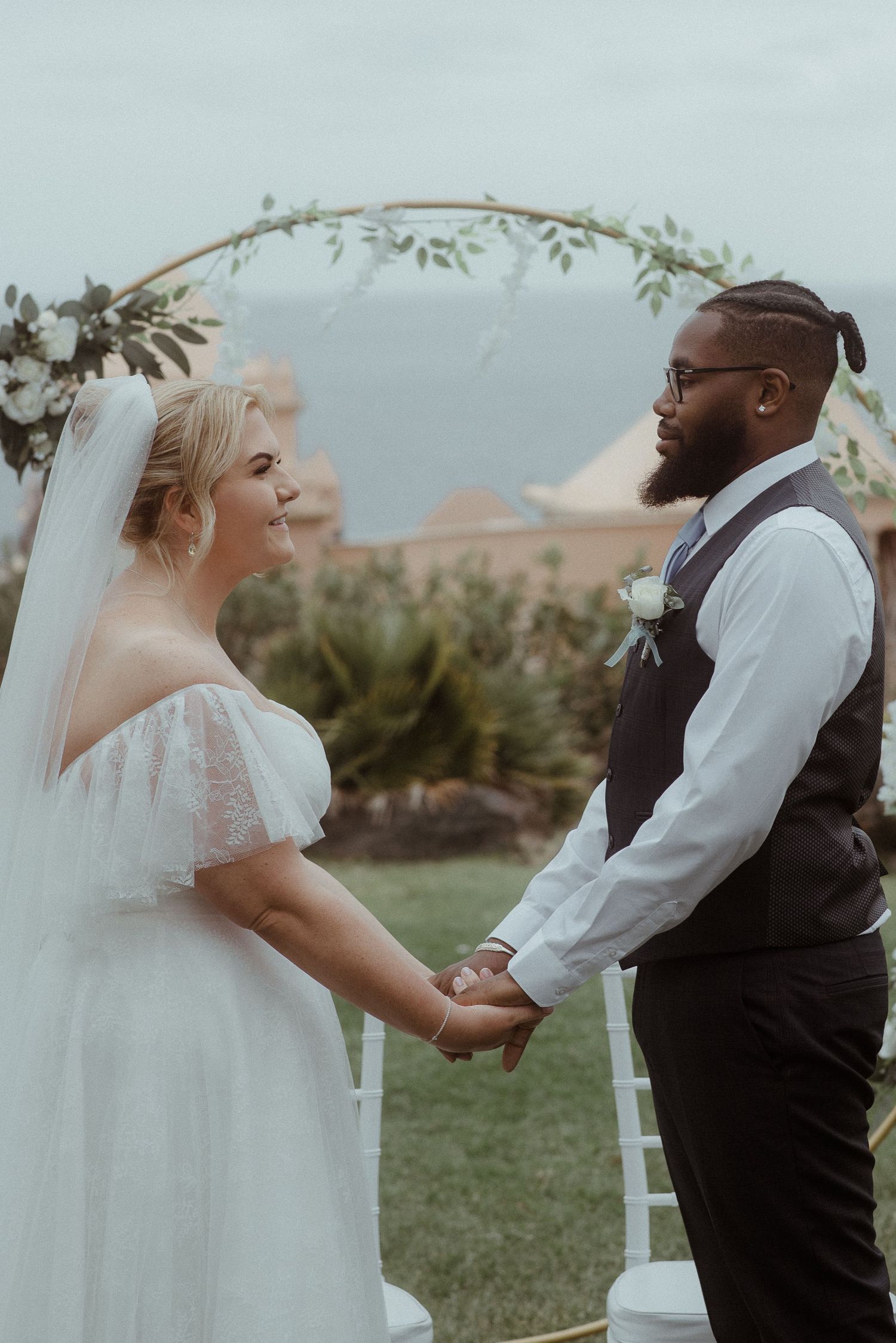 Couple exchanges vows during outdoor garden ceremony under floral arch.