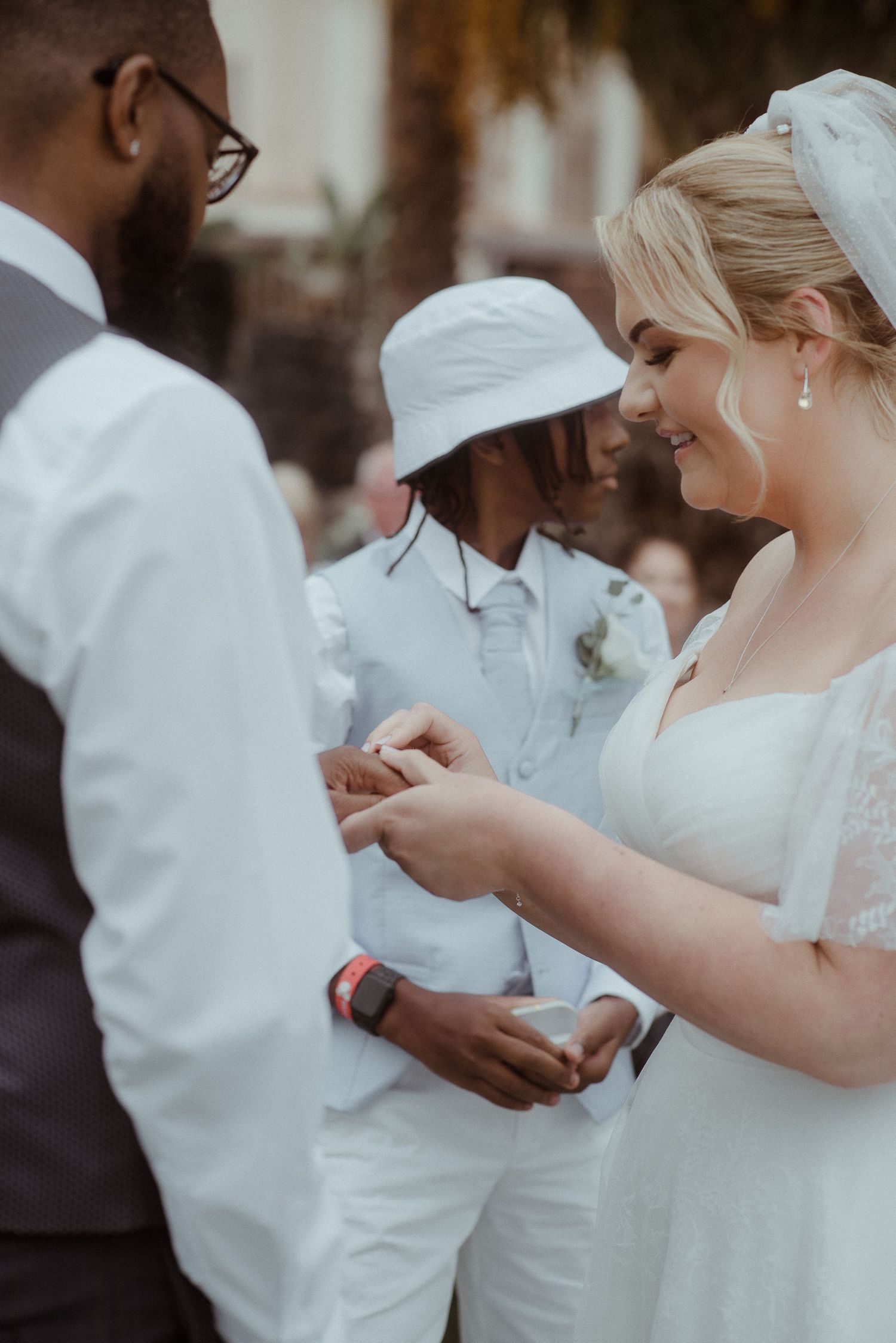 Wedding ceremony ring exchange moment with guests in background.