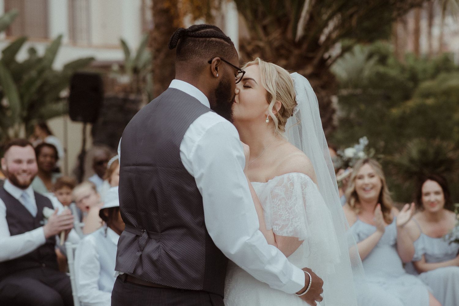 Newlyweds share their first kiss as guests applaud in background.