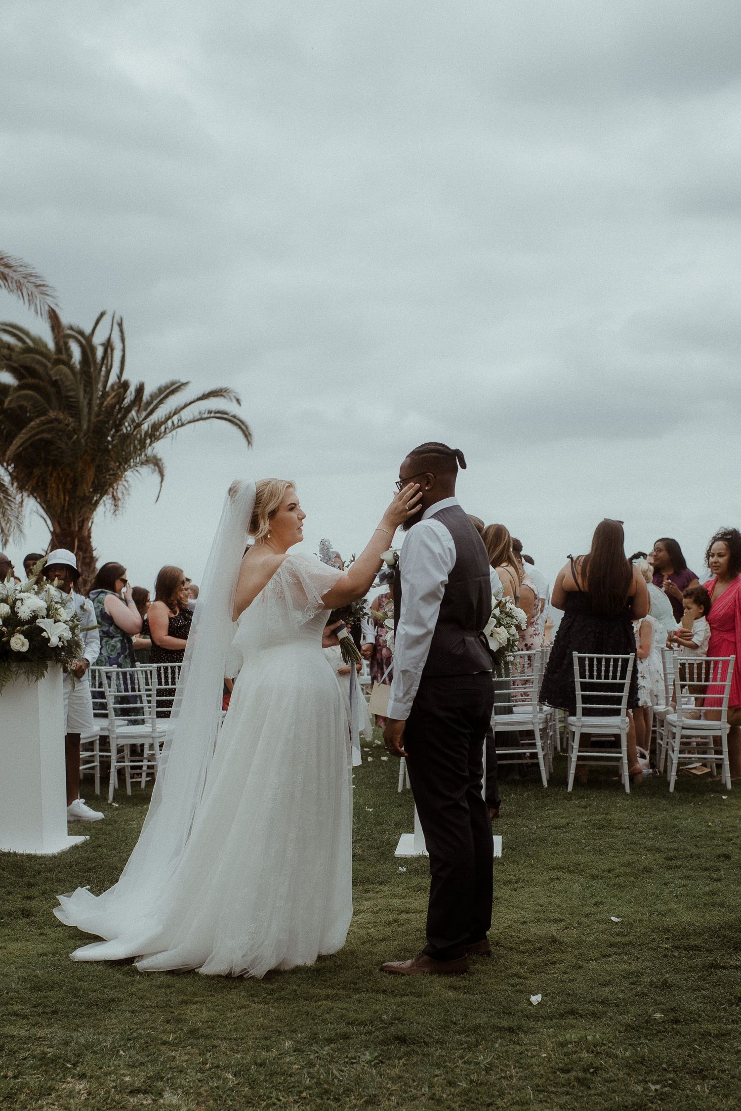 Joyful celebration at outdoor wedding with white chairs and tropical landscaping.