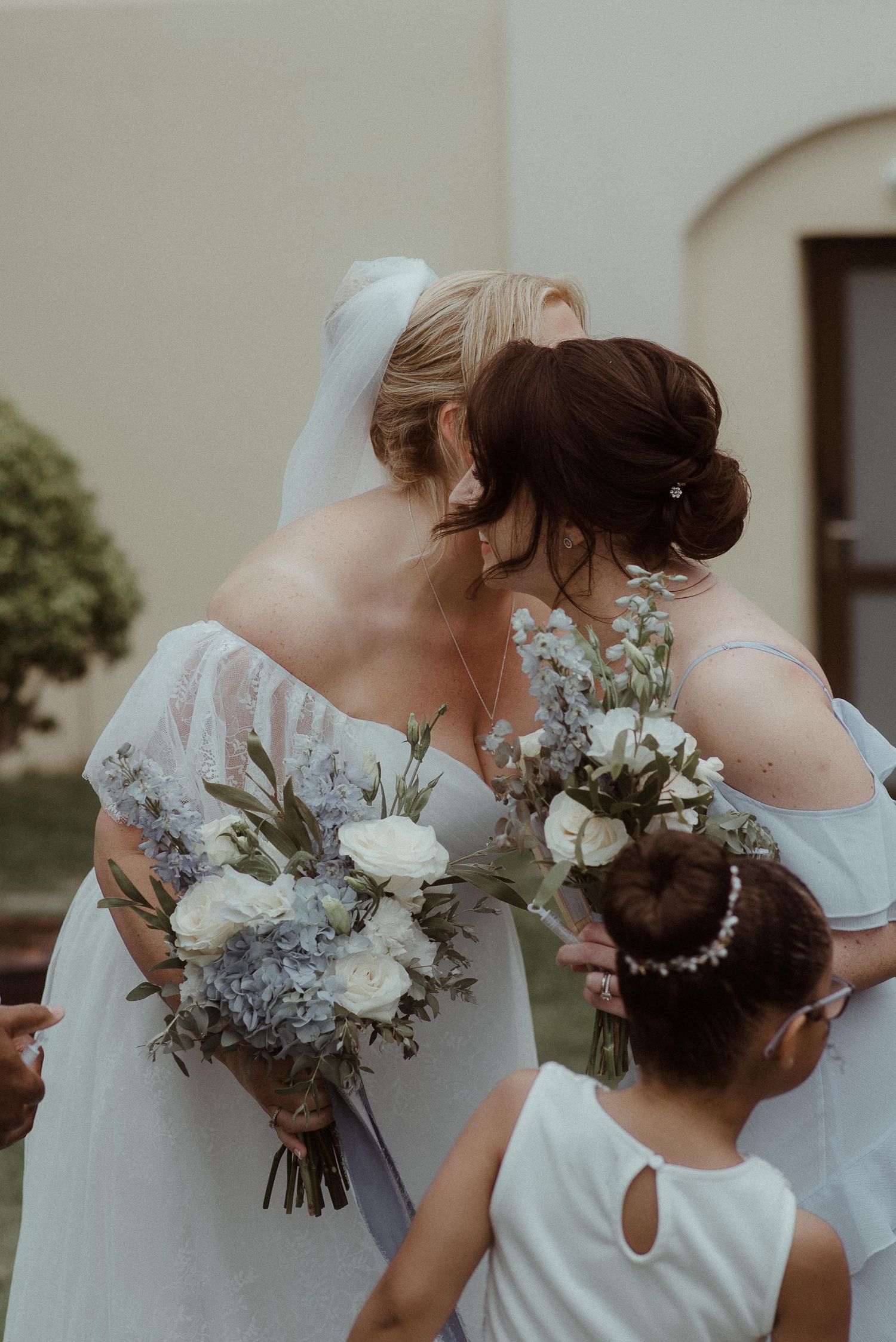 Wedding party with pastel bouquets and off-shoulder dresses pose together outdoors.