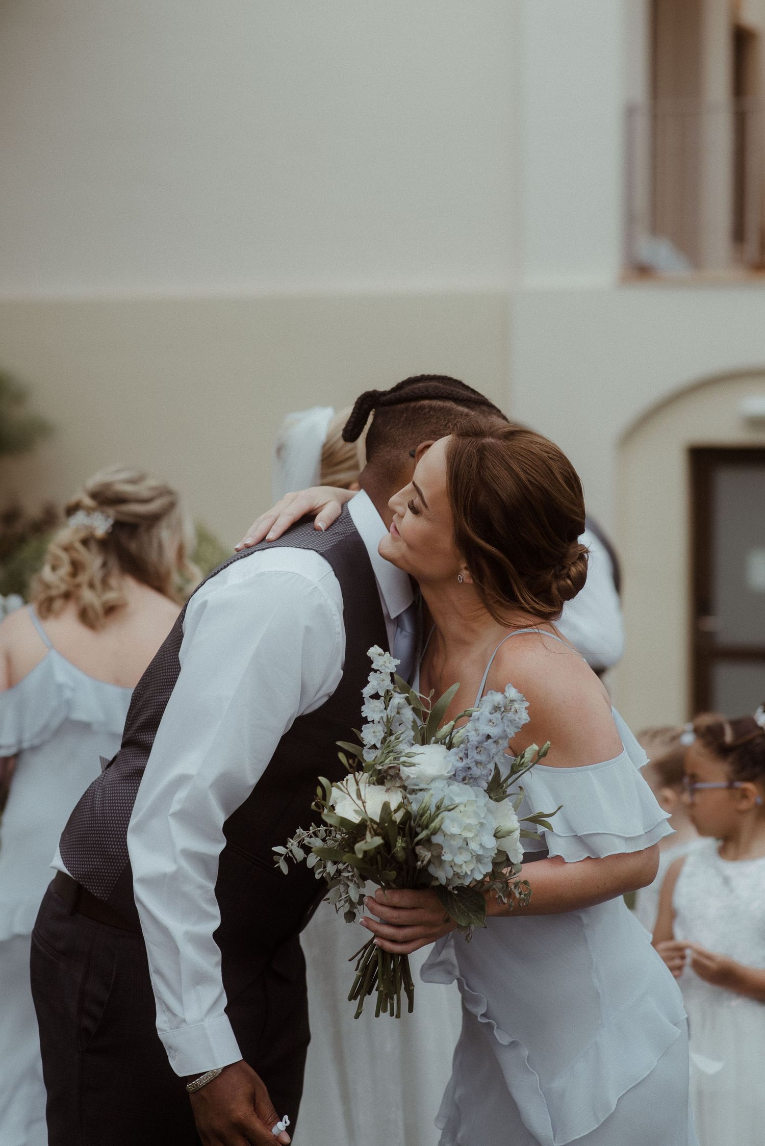 A romantic moment at a wedding ceremony with the couple sharing a kiss while holding a bouquet of white and blue flowers.