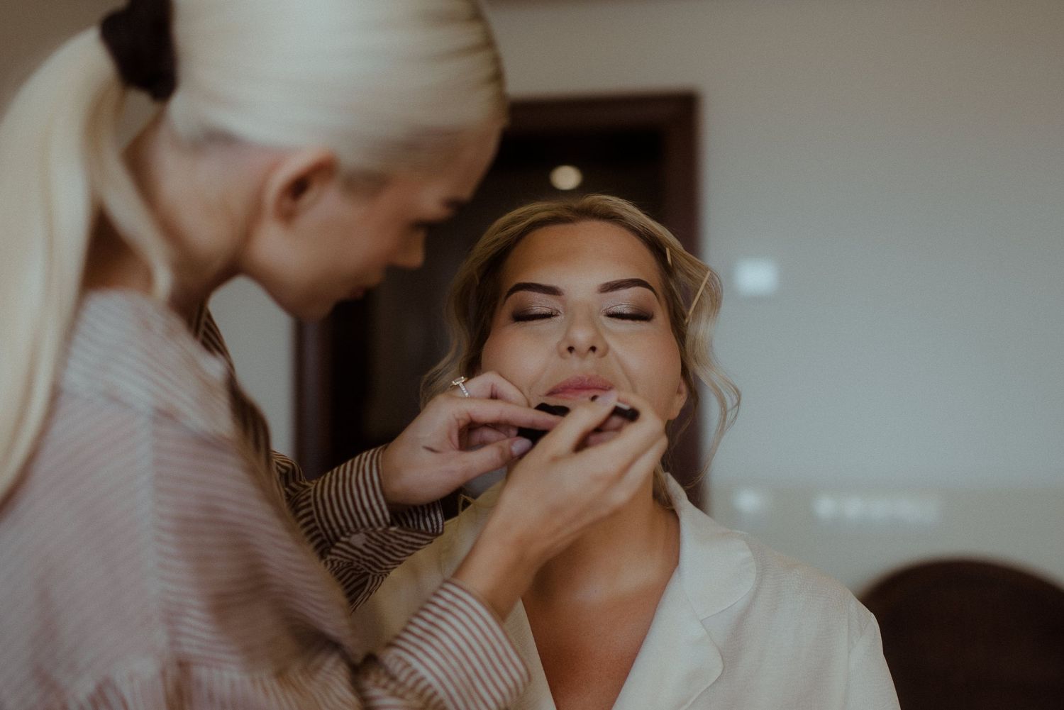 Close-up shot of bridal makeup application in soft, moody lighting.