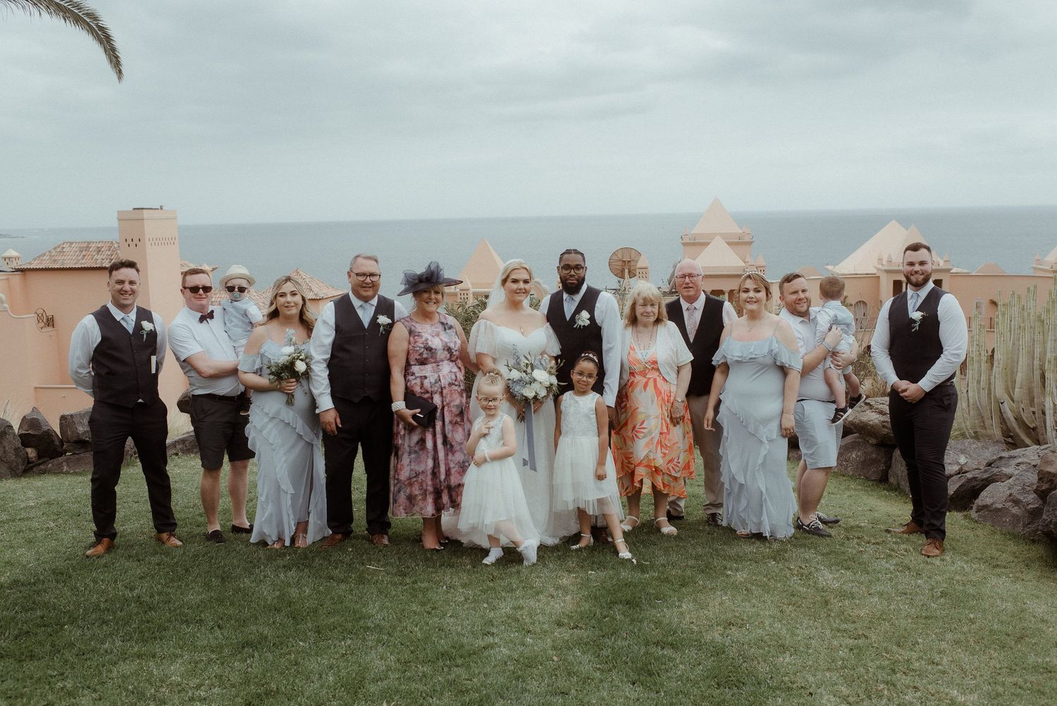 Wedding party group shot with coastal views and pink Spanish-style architecture.