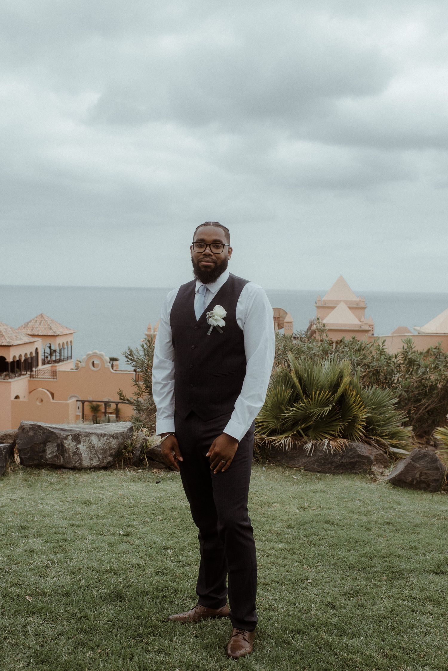 Formal portrait of wedding attendant on grounds of seaside resort with Mediterranean architecture.