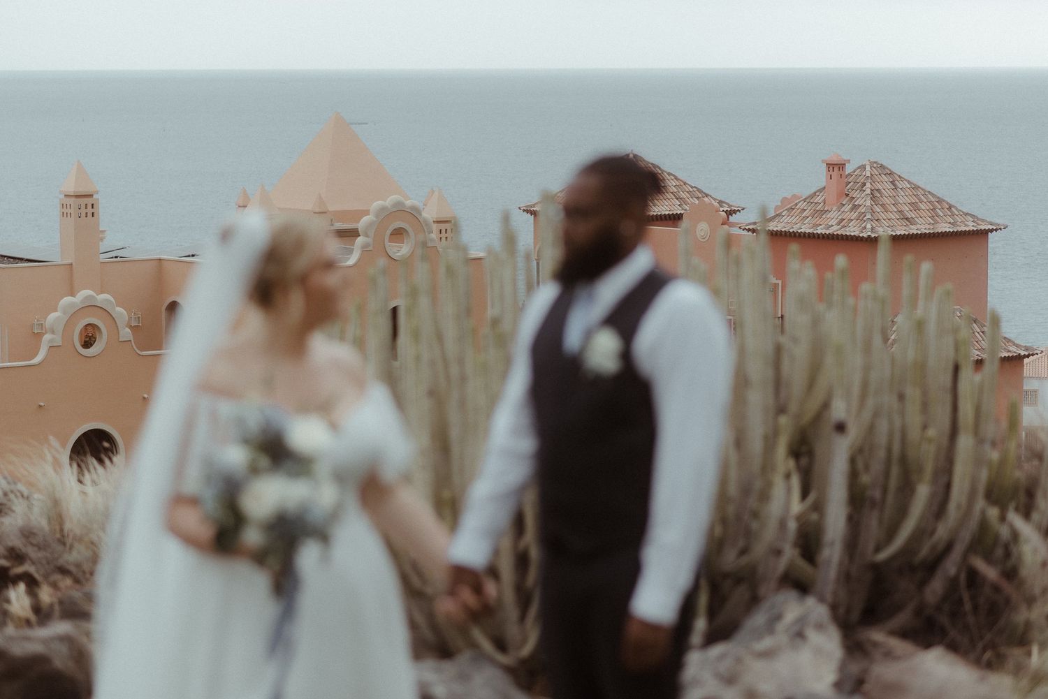 Newlyweds share intimate moment with Mediterranean architecture in background.