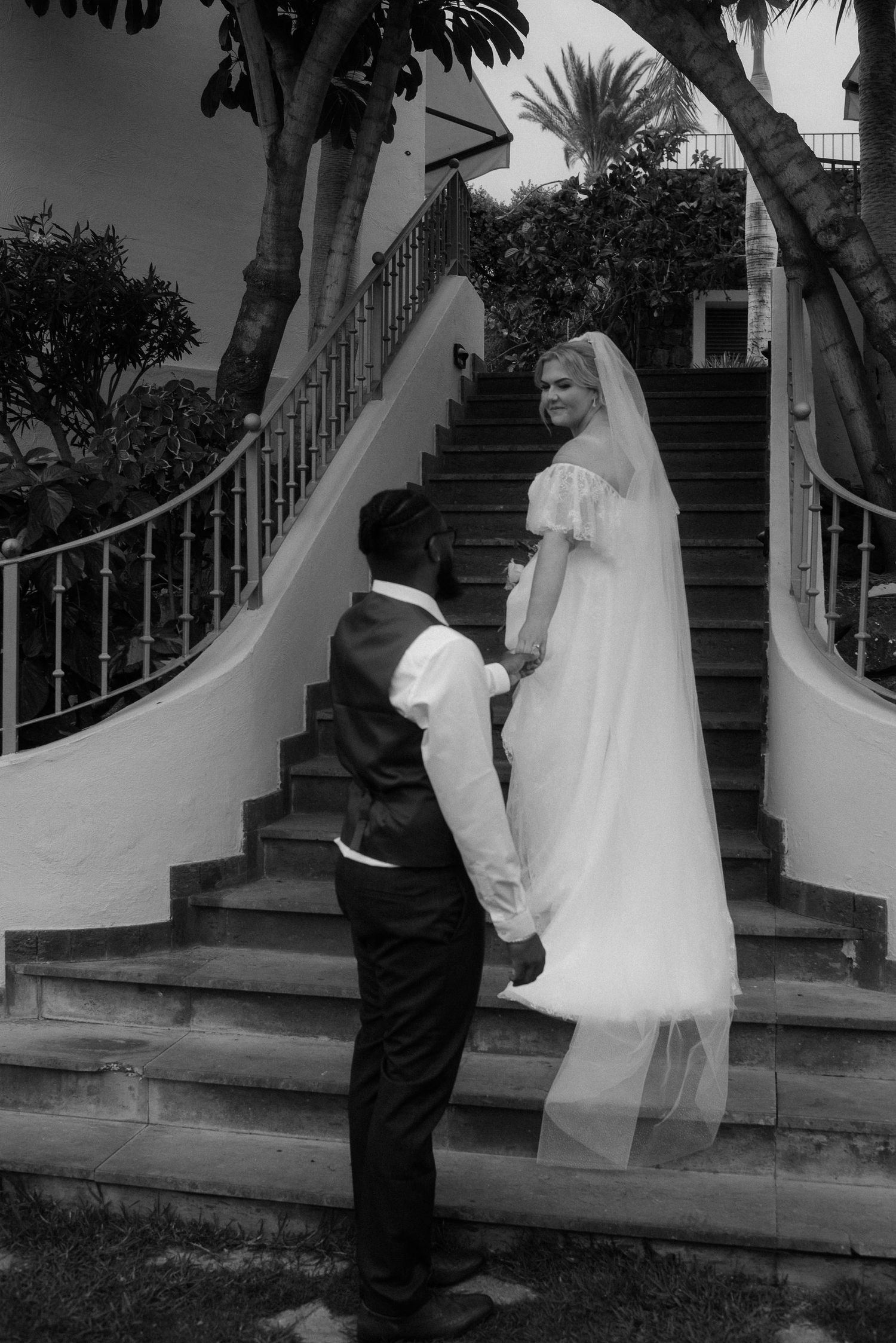 Black and white wedding portrait on elegant curved staircase with tropical foliage.
