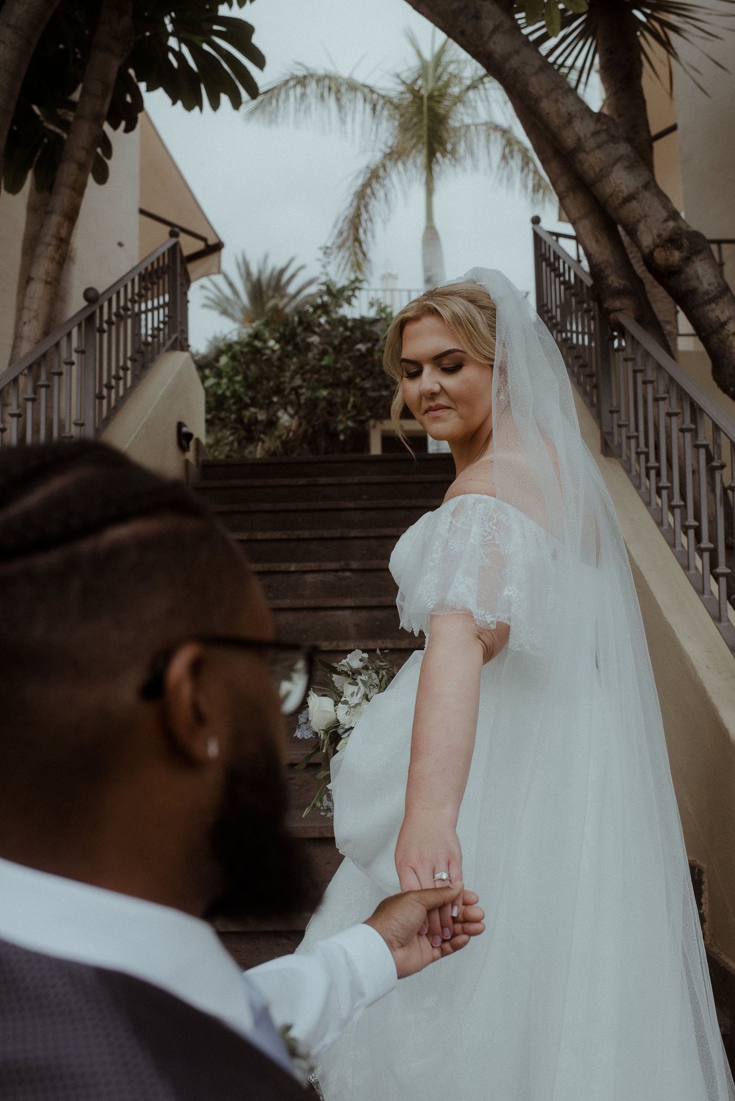 Romantic moment captured on ornate staircase with palm trees framing the scene.