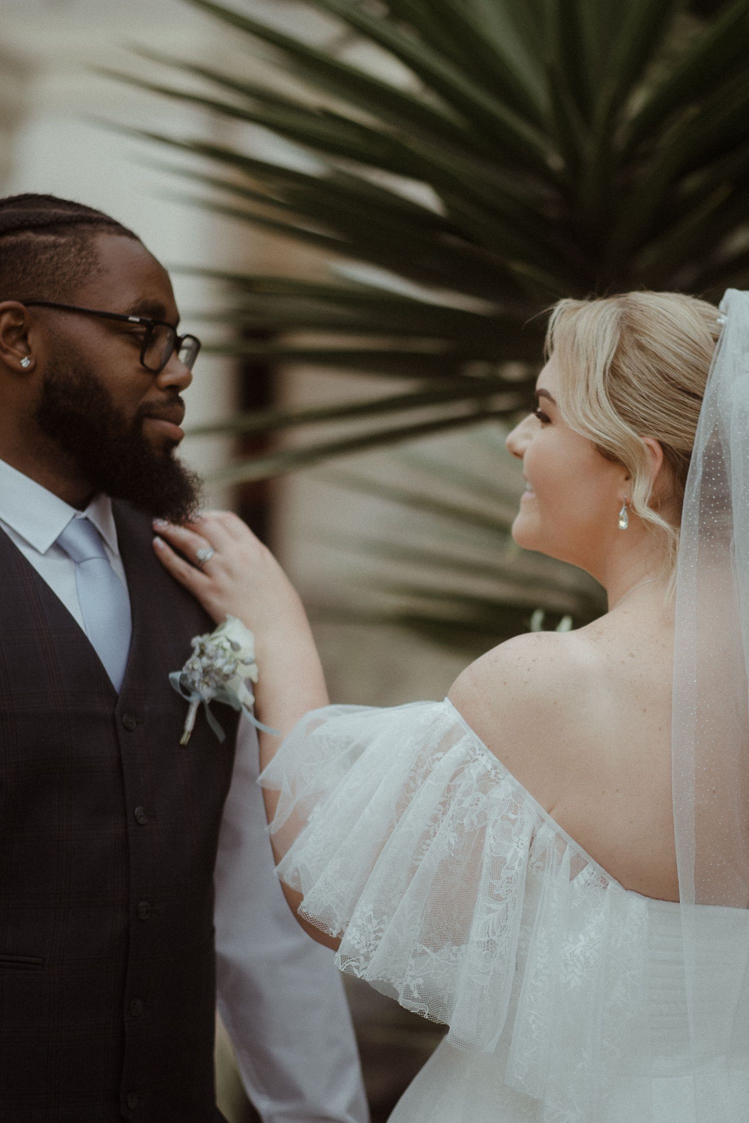 Intimate wedding moment captured with palm fronds in background as couple shares tender interaction during ceremony.