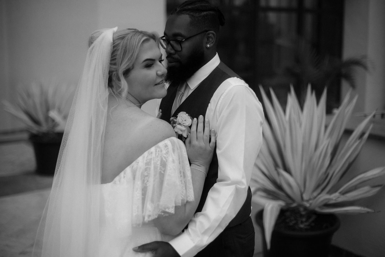 Black and white wedding photo with tropical plants framing intimate moment between couple.