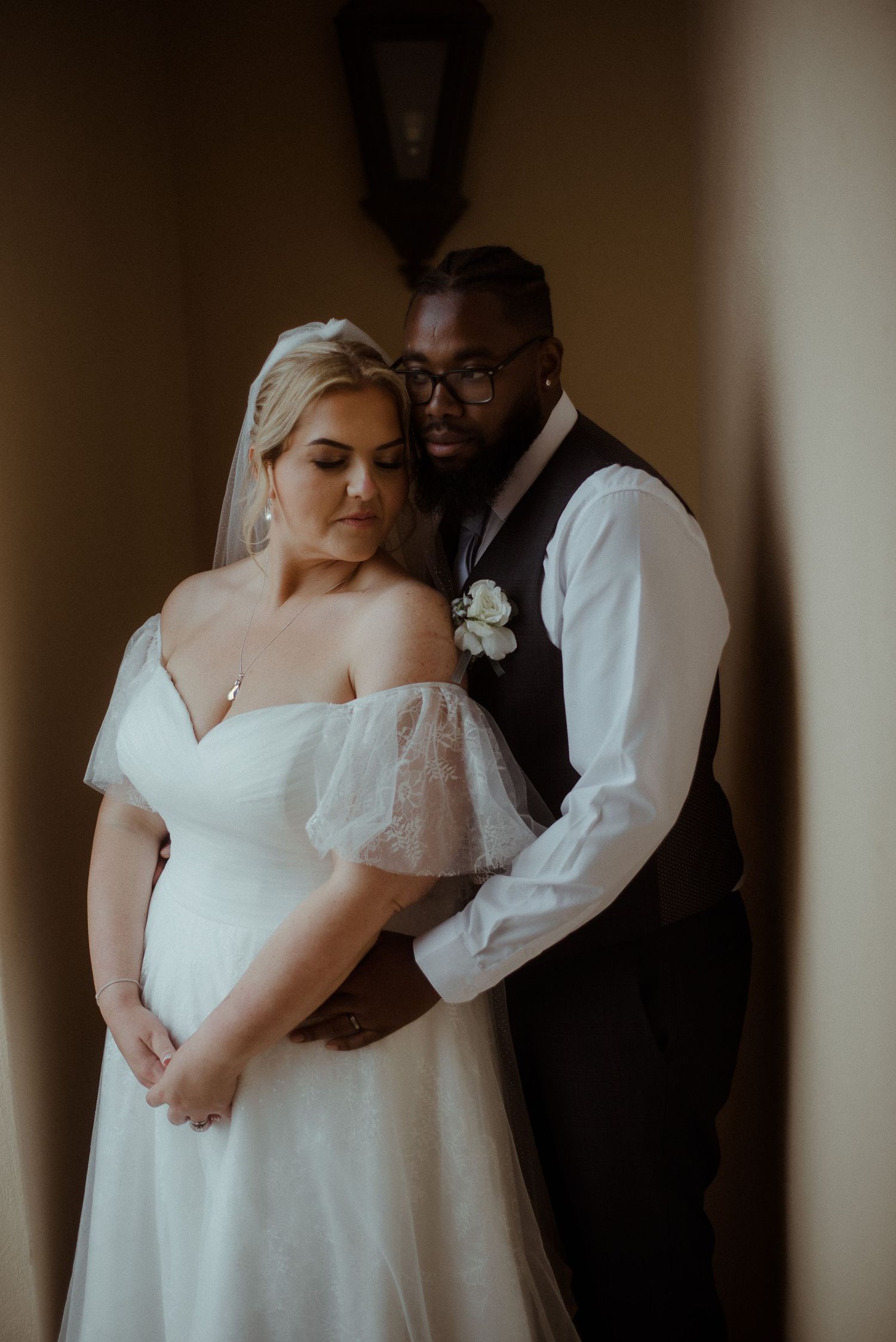 Moody indoor wedding portrait captures tender embrace between newlyweds.