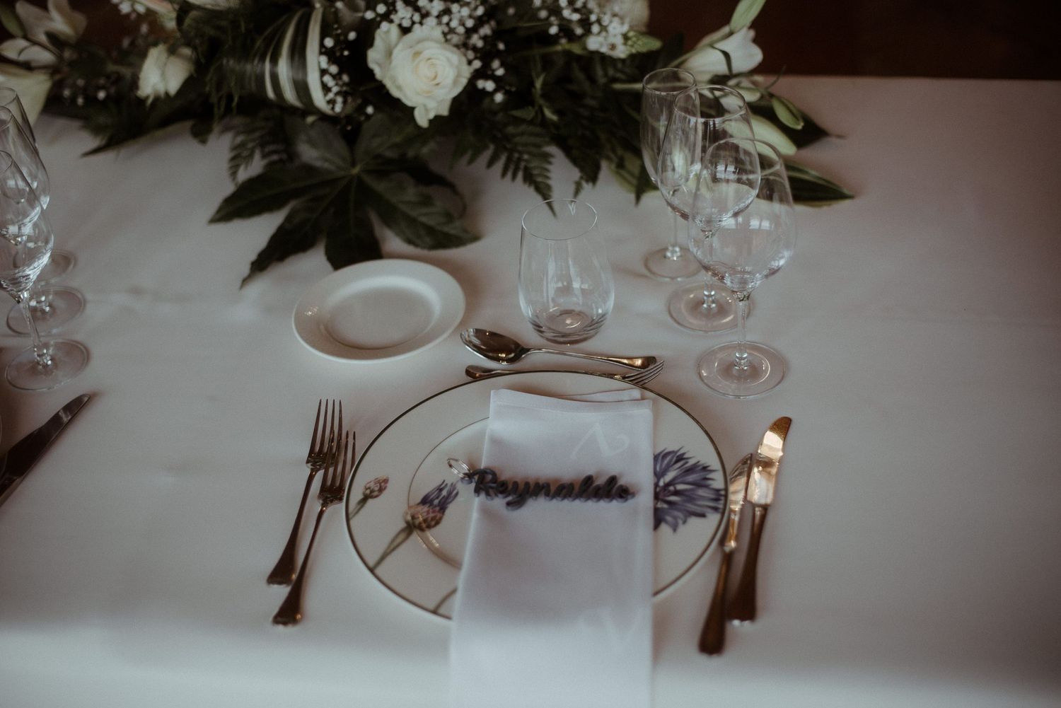 Elegant wedding table setting with white napkin, fine china, and floral centerpiece.