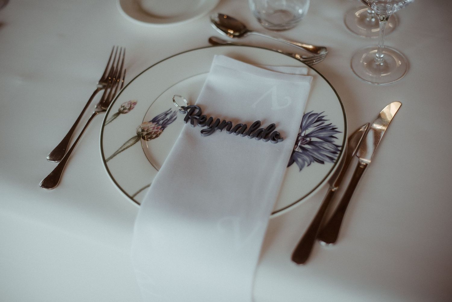 Close-up of formal place setting with embroidered napkin and gold cutlery at wedding reception.