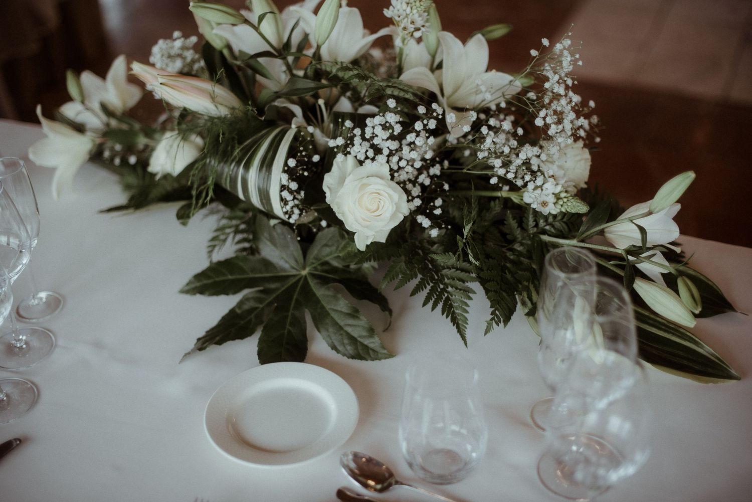 White and green floral centerpiece with roses and baby's breath on wedding reception table.