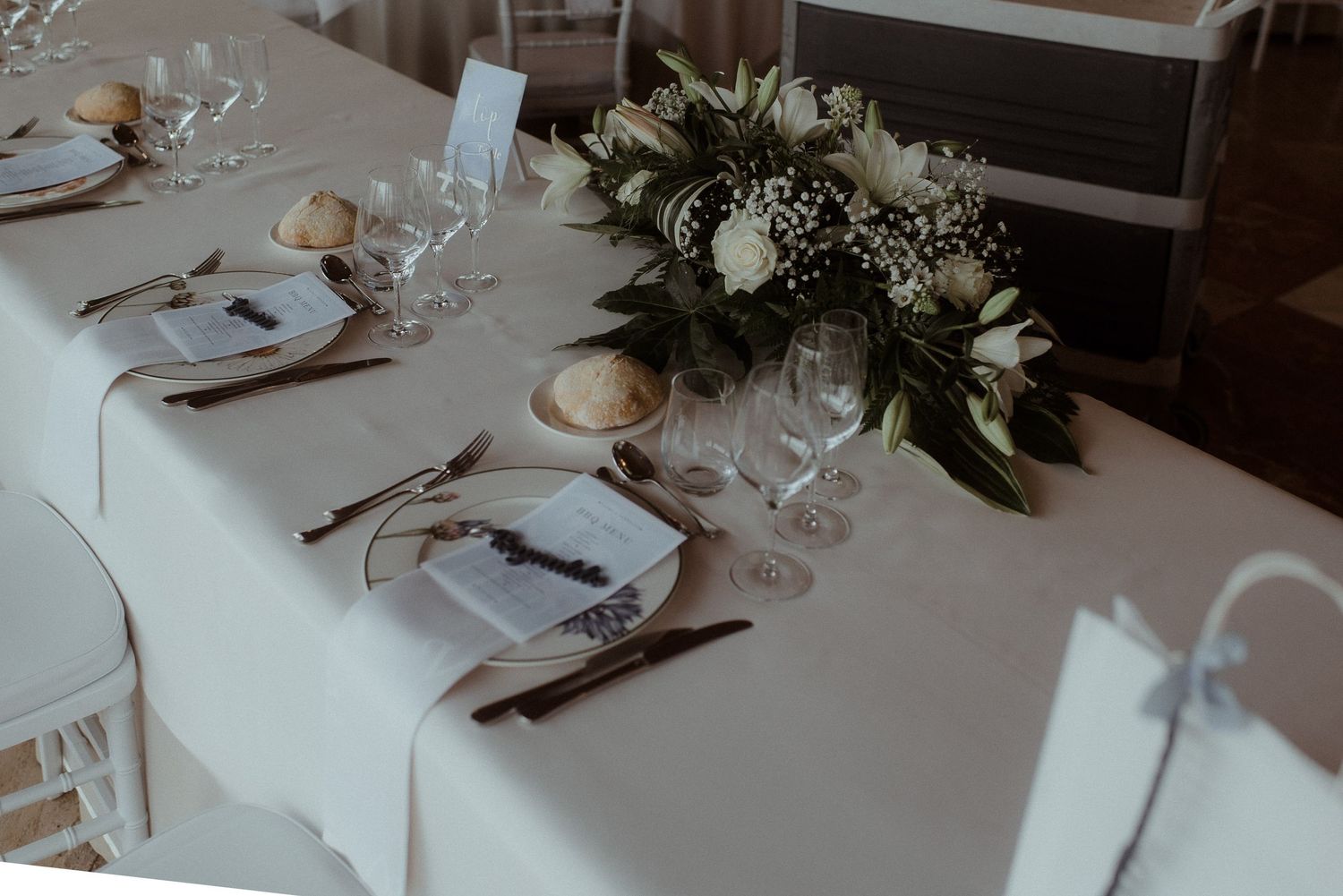 Wedding reception table with elegant place settings and white floral centerpiece.