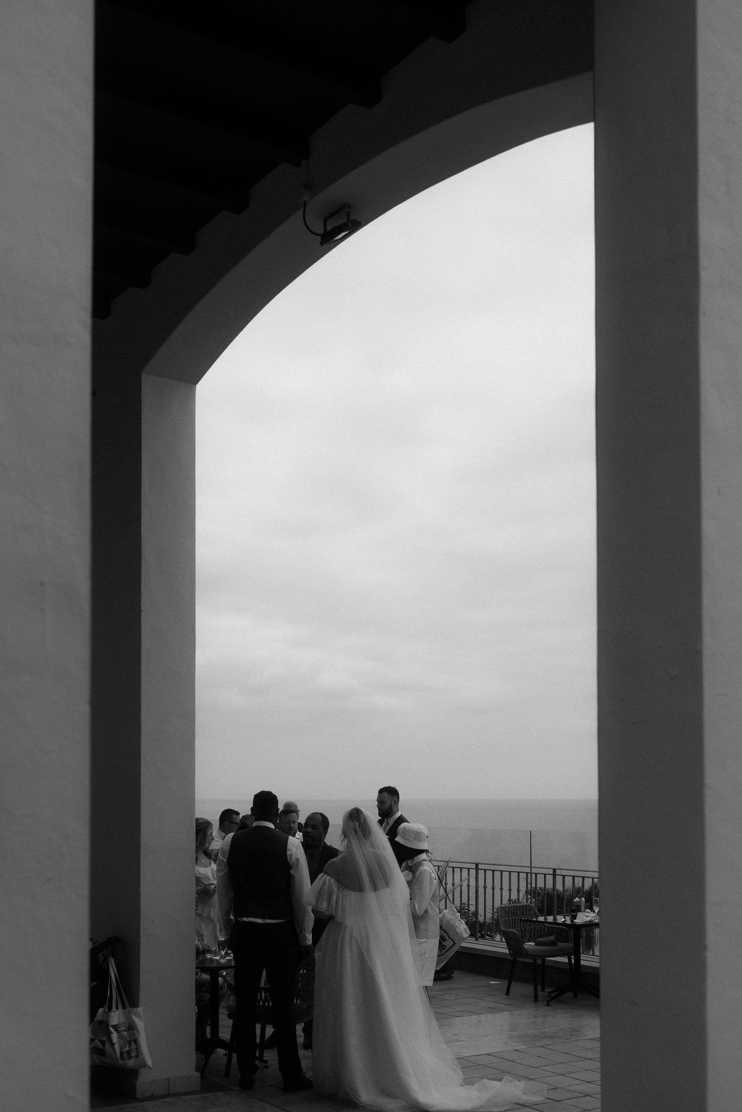 Wedding ceremony silhouetted through arched doorway overlooking ocean view.