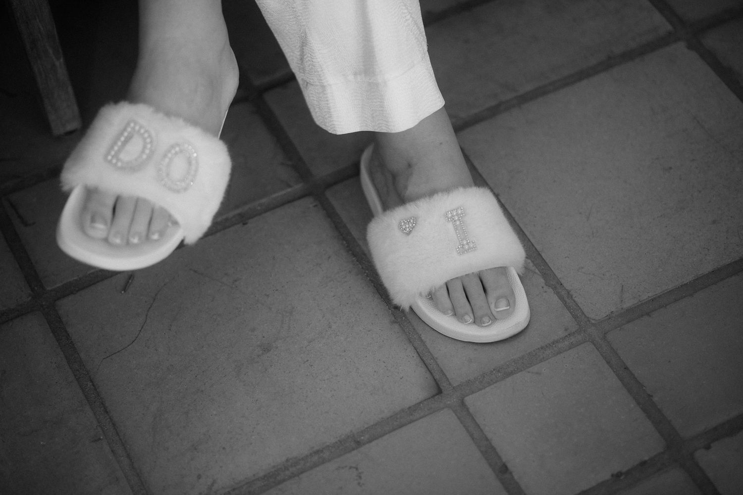 Feet wearing white spa slippers on gray tiled floor.