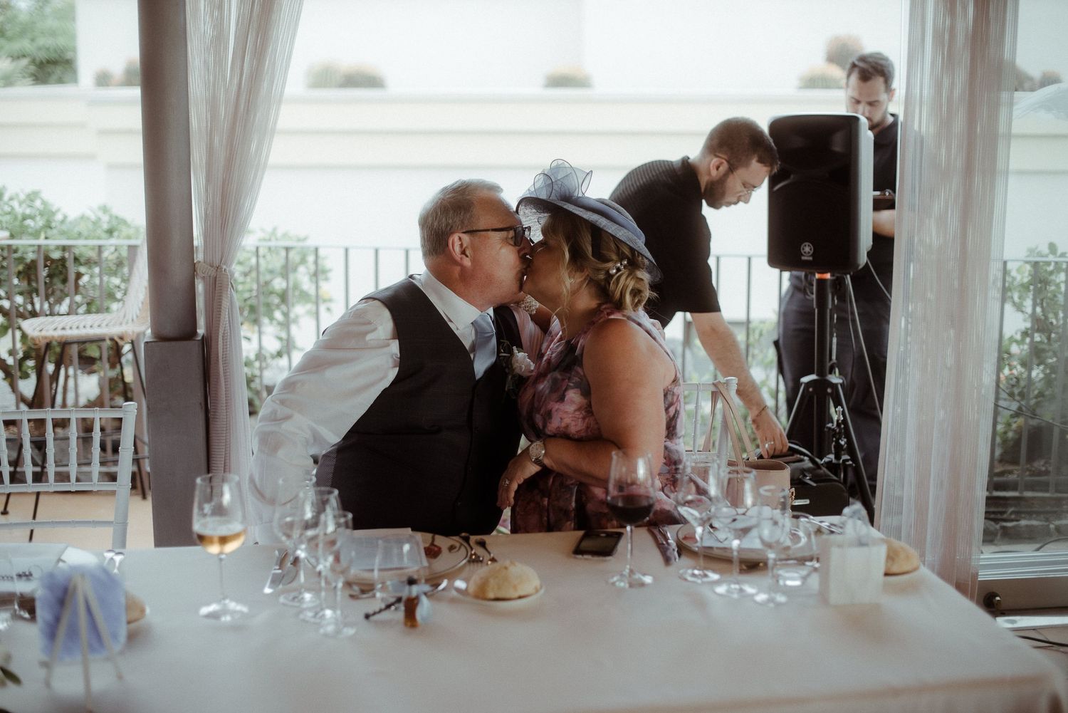 A tender moment shared between elegantly dressed guests at a wedding reception under a covered tent.