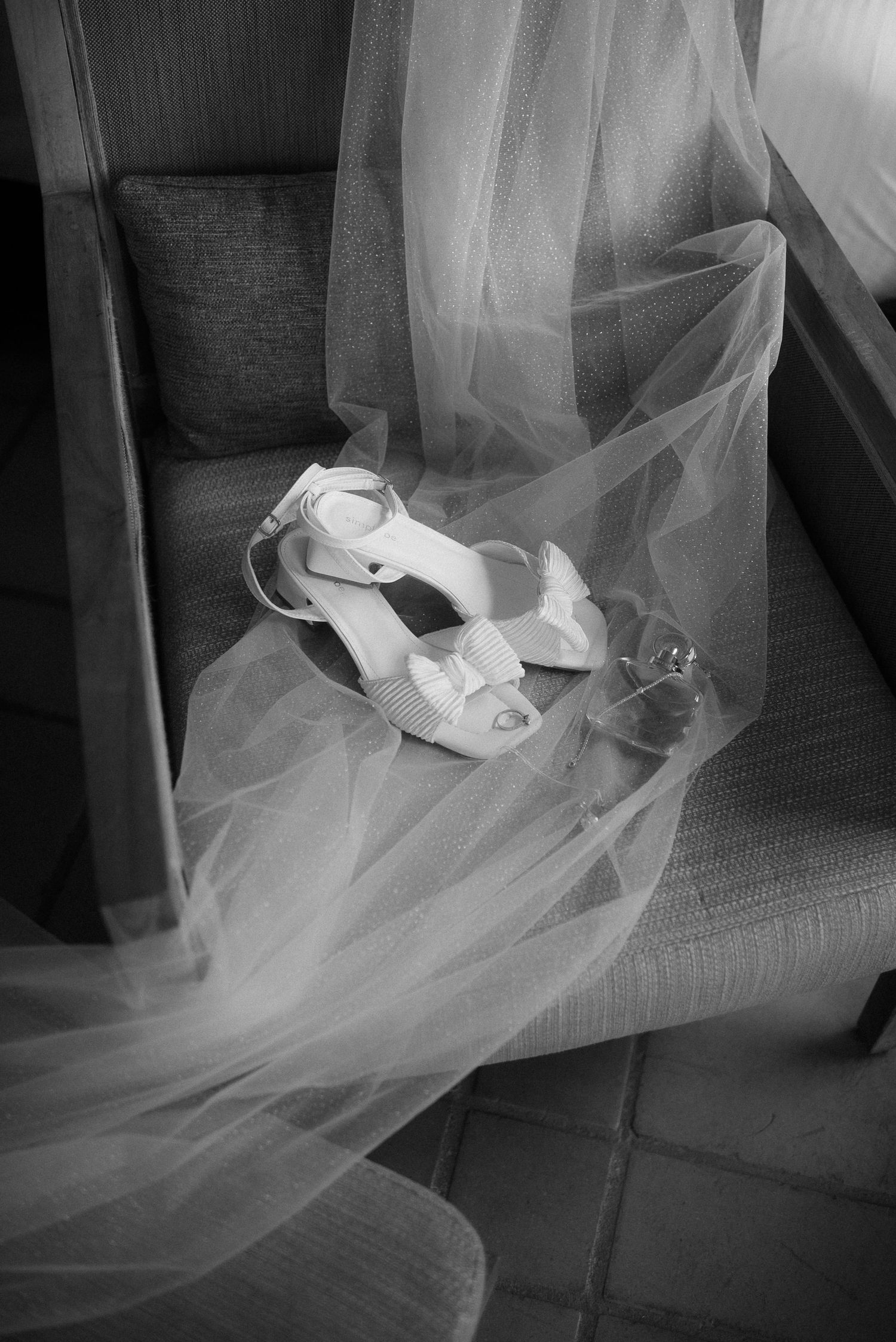 White wedding heels resting on delicate tulle veil on a gray chair.