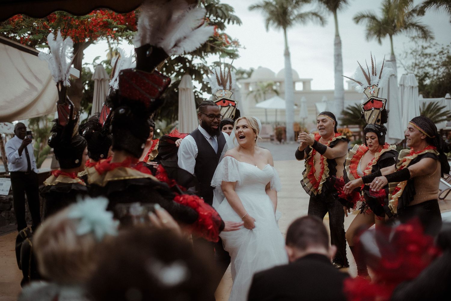 Wedding celebration features traditional dancers in ornate costumes performing around newlyweds outdoors.