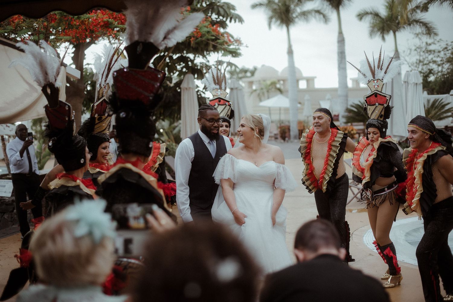 Traditional dancers in colorful costumes perform around wedding couple during outdoor reception.