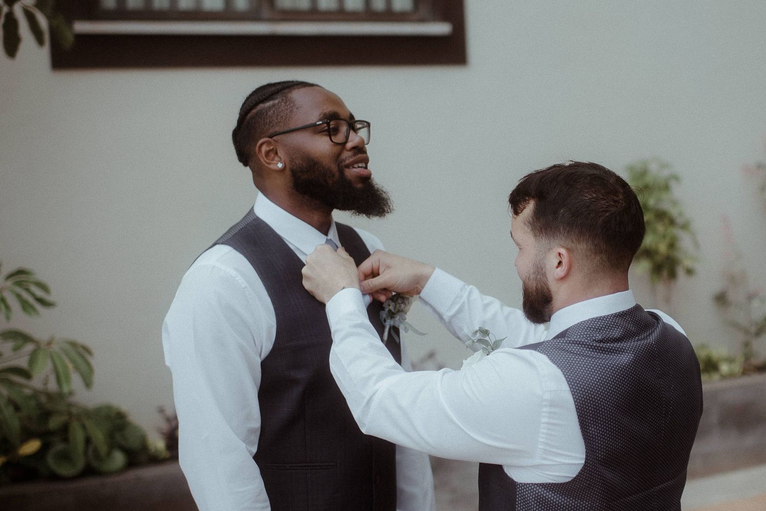 Two groomsmen helping each other with formal attire adjustments.