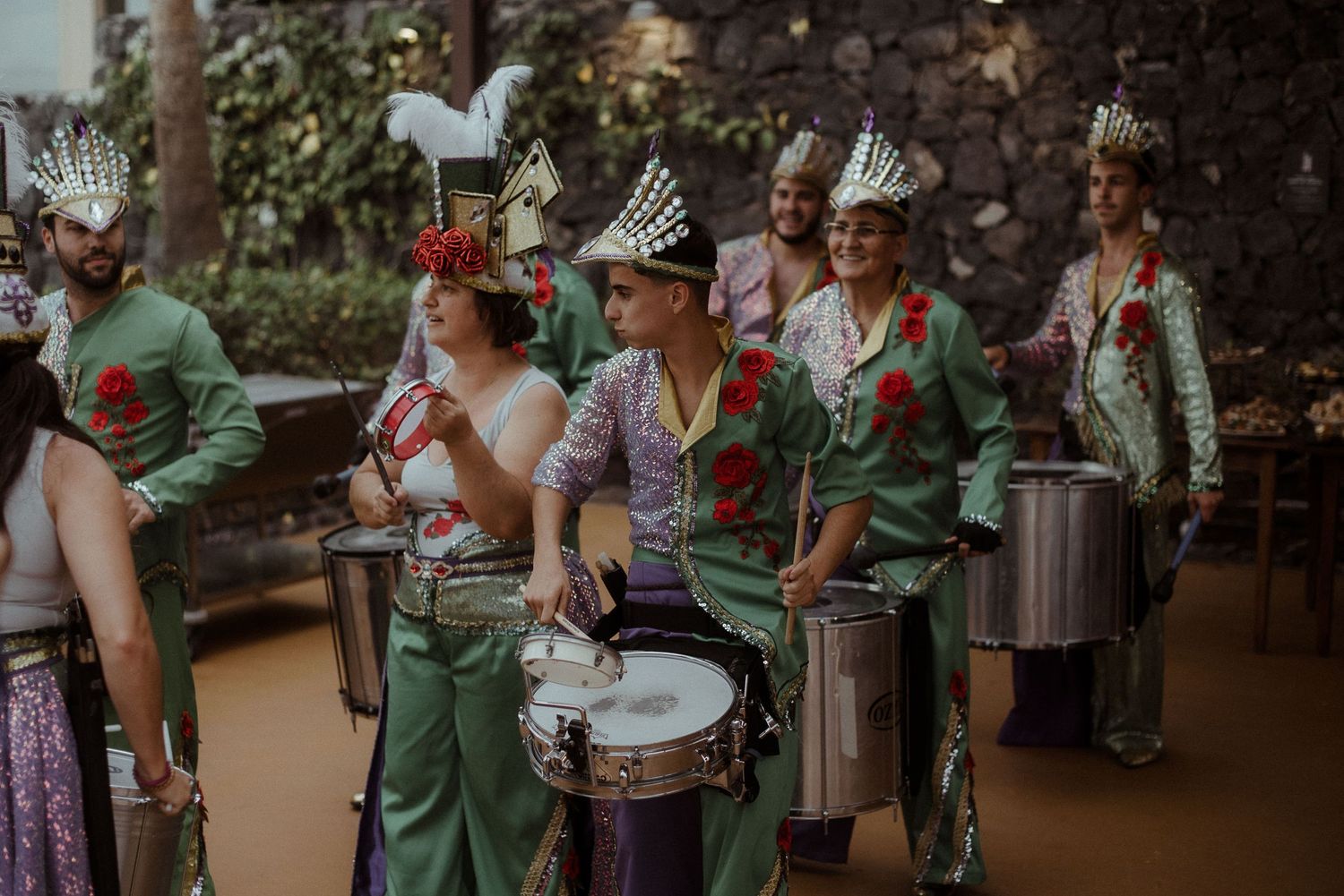 Marching band members in green uniforms play drums during an outdoor performance.