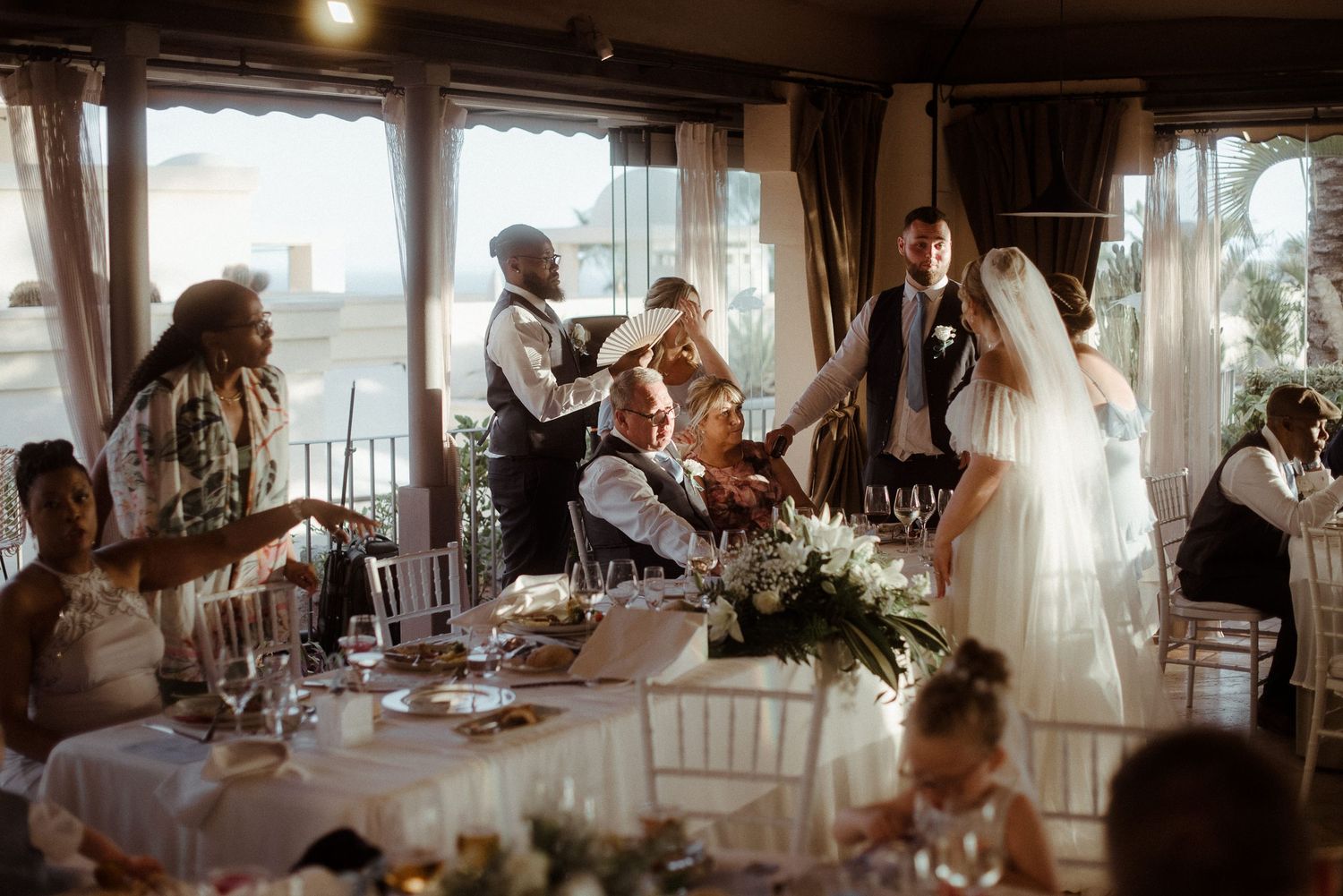 Reception guests mingle and toast around white-clothed dining tables.