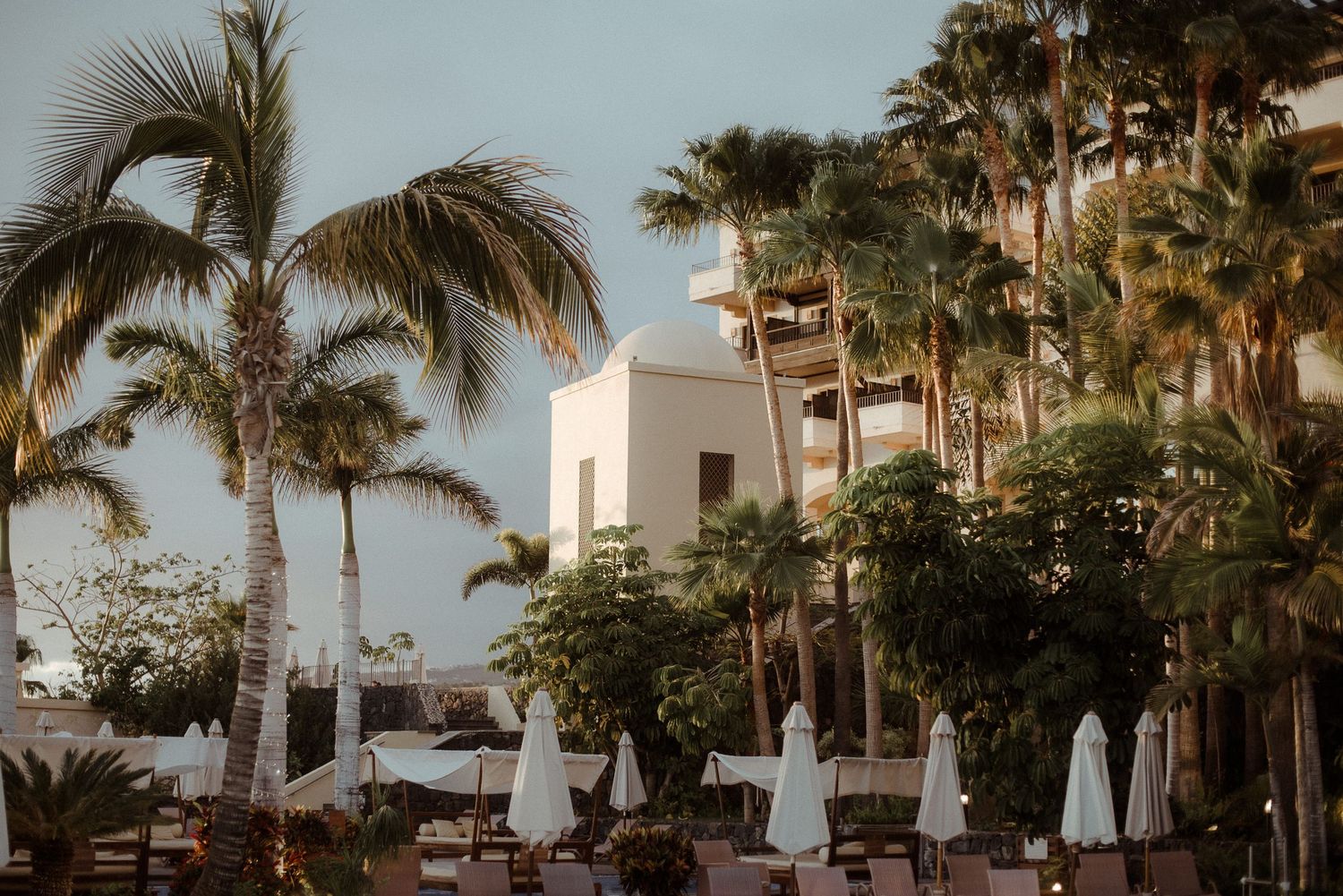 Palm trees frame a white Mediterranean-style building at sunset.