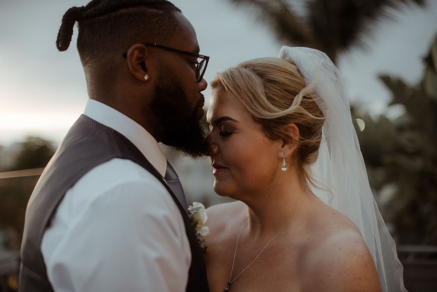 Close-up of newlyweds sharing an intimate moment against palm trees.