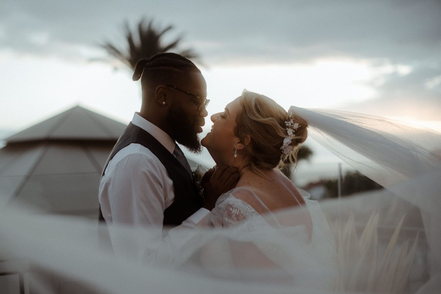 Romantic portrait of newlyweds with flowing veil in soft lighting.