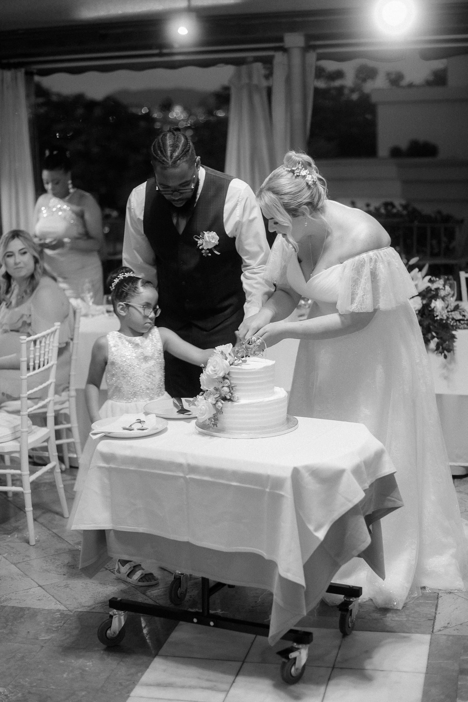 Black and white photograph of a couple cutting their wedding cake during the reception.