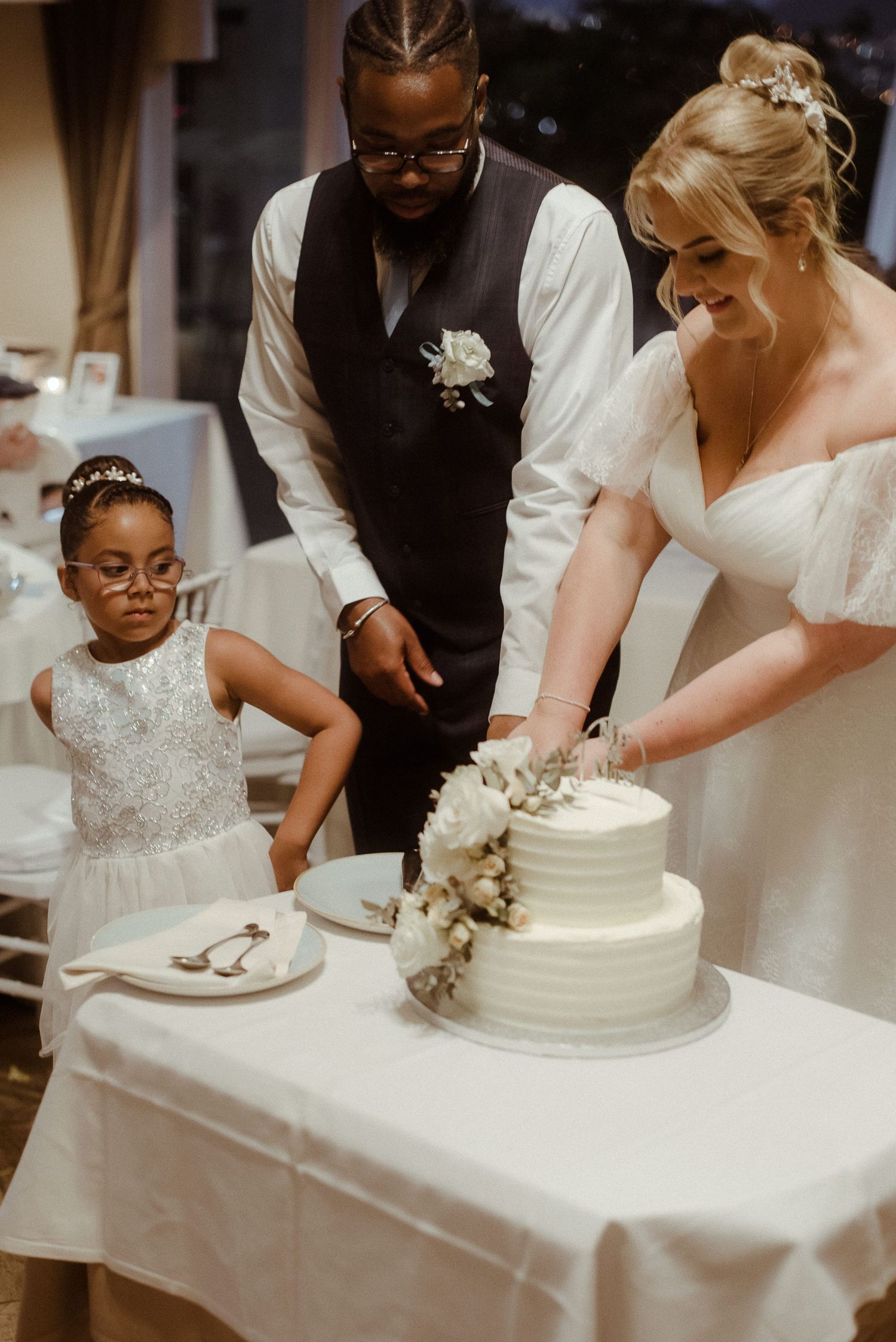 Wedding cake cutting moment with a young attendant watching at an indoor reception.
