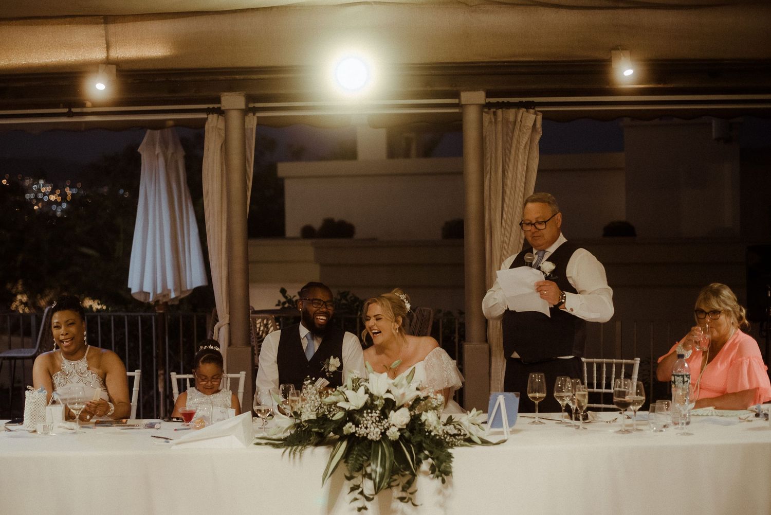 Wedding reception head table with floral centerpieces and white linens.