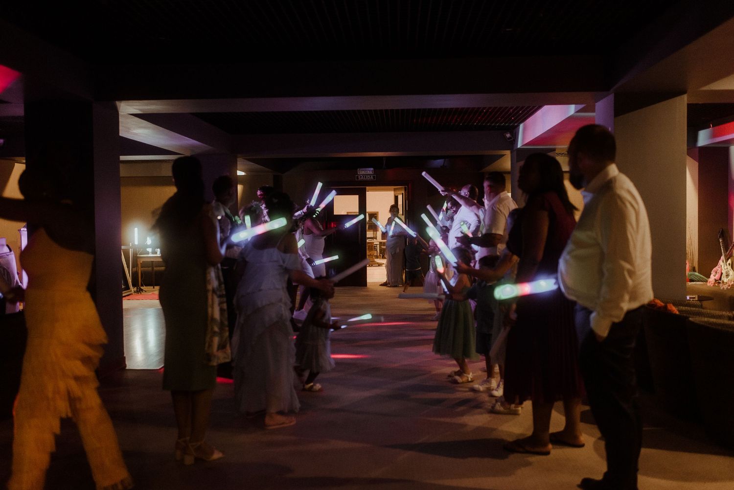 Wedding guests forming a tunnel with glowing light sticks during evening celebration.