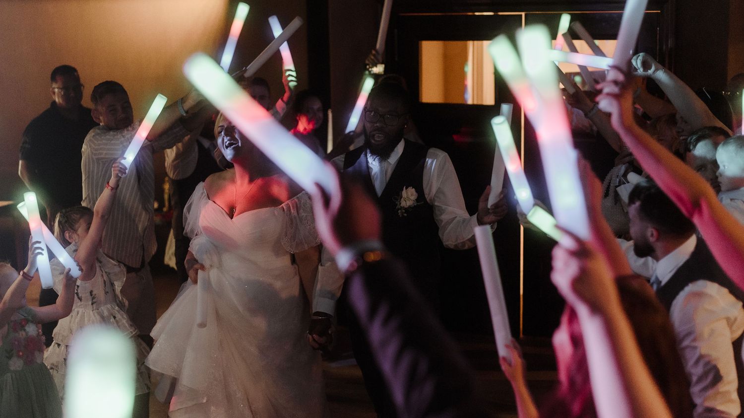 Dance floor celebration with guests holding illuminated glow sticks at wedding reception.